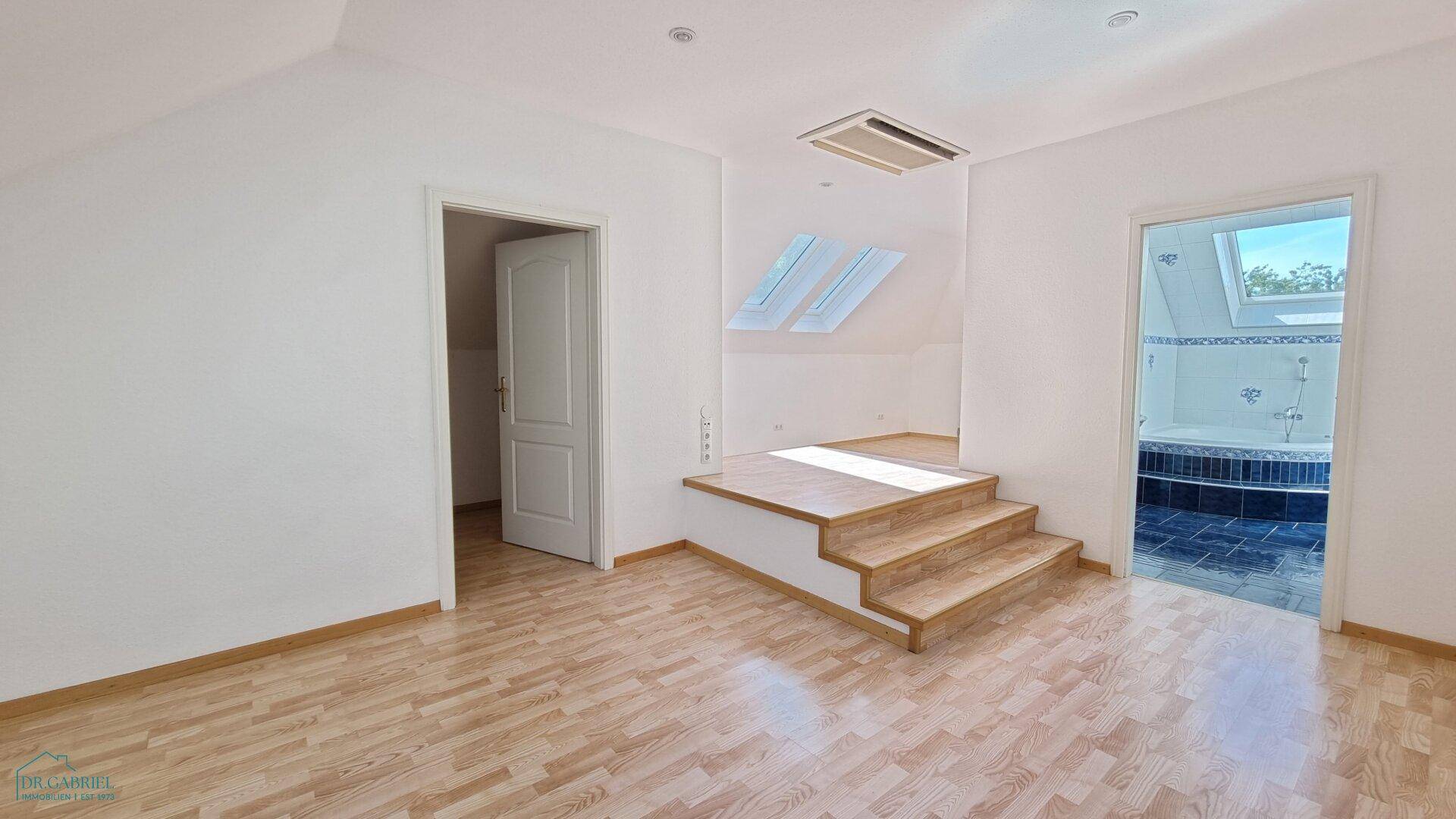 Dachbodenraum mit Laminatboden, schrägen Decken und Zugang zu einem Badezimmer mit Eckbadewanne.