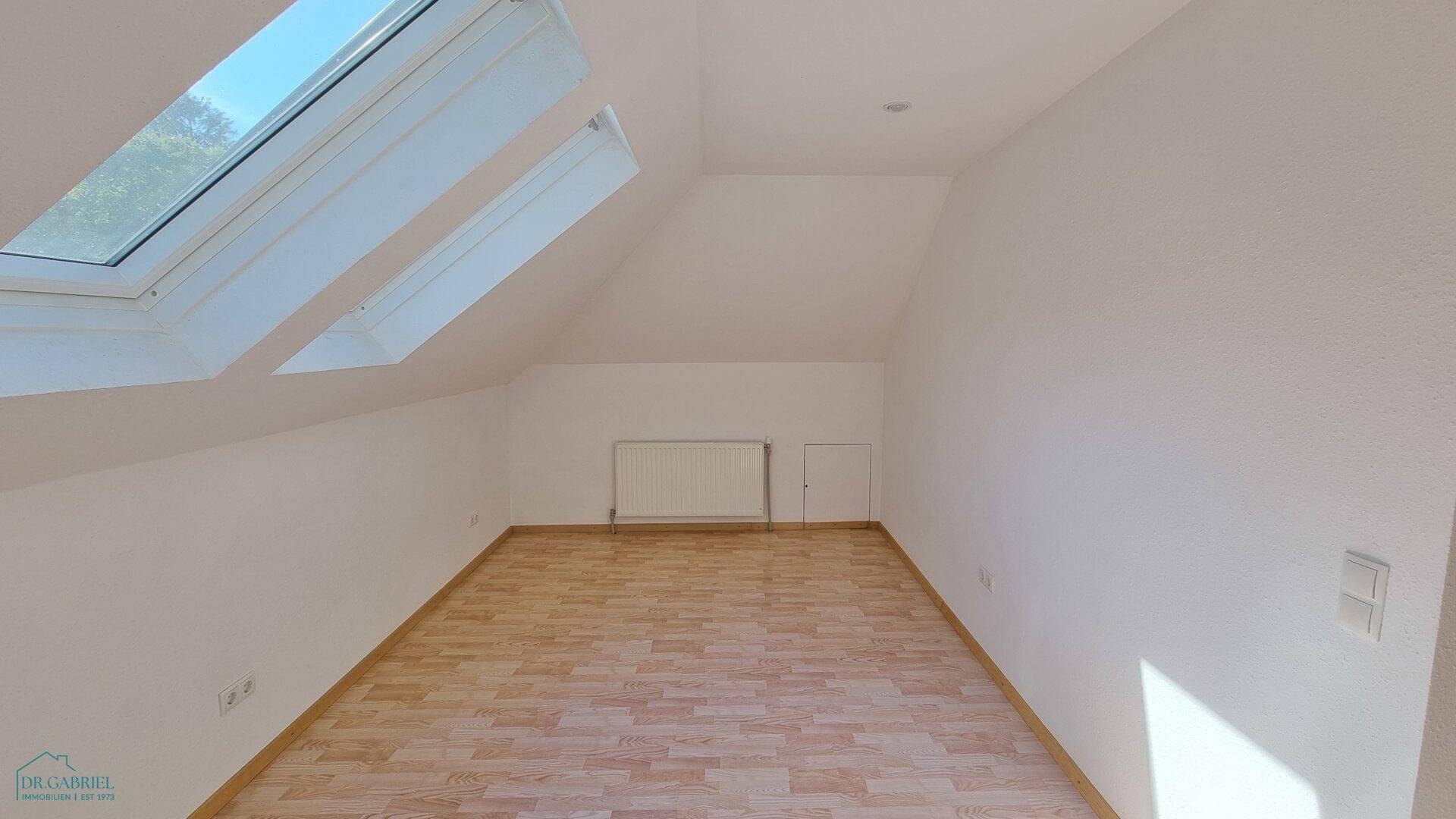 Geräumiger Dachbodenraum mit hellem Laminatboden und zwei großen Dachfenstern für viel Tageslicht.