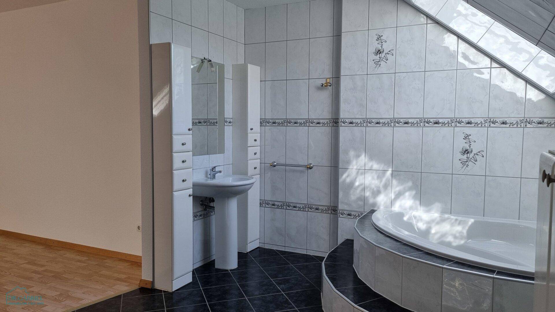 Badezimmer mit Standwaschbecken, Spiegelschrank und gefliesten Wänden, teilweise mit Eckbadewanne.