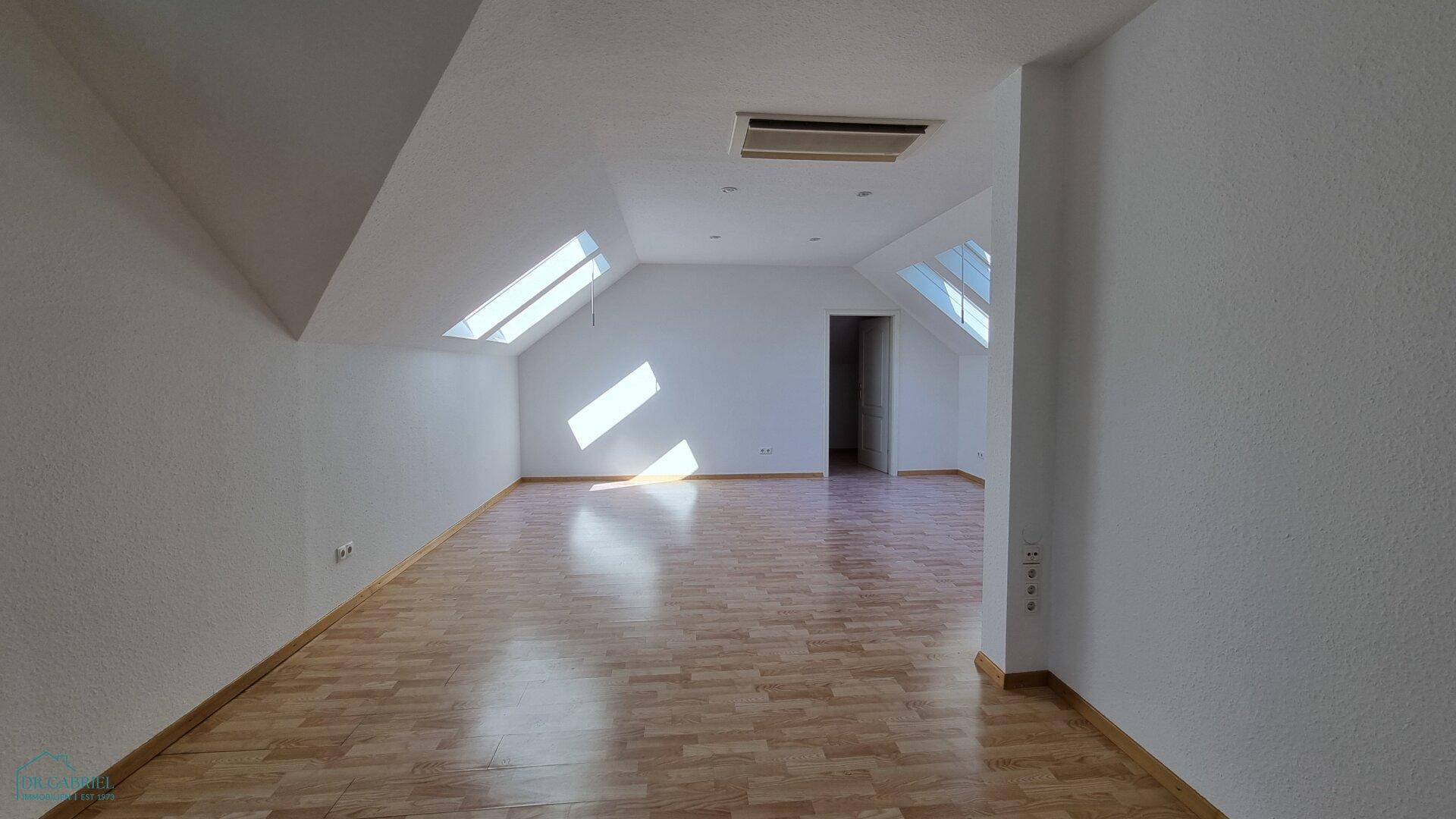 Großer, heller Dachbodenraum mit Laminatboden und mehreren Dachfenstern, die viel Sonnenlicht hereinlassen.