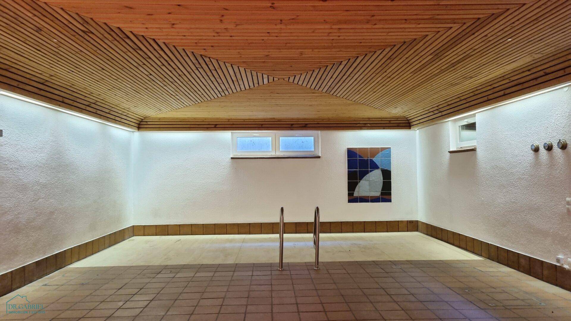 Innenpoolbereich mit gefliestem Boden, weiß gestrichenen Wänden und einer markanten Holzlamellendecke.