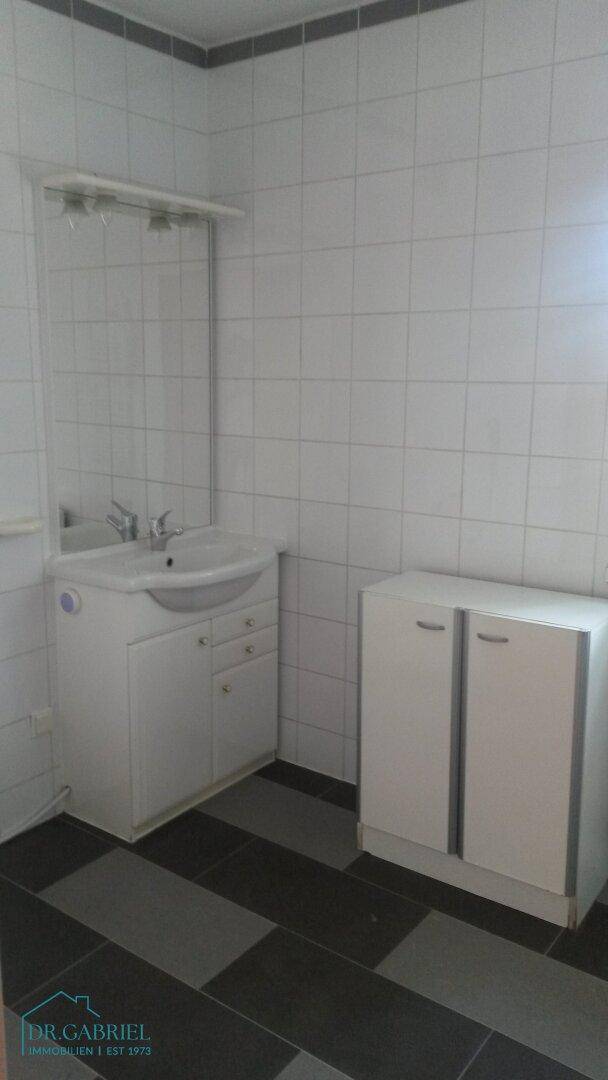 Badezimmer mit Waschbecken, Spiegel und weißen Fliesen, ergänzt durch einen gemusterten Boden.