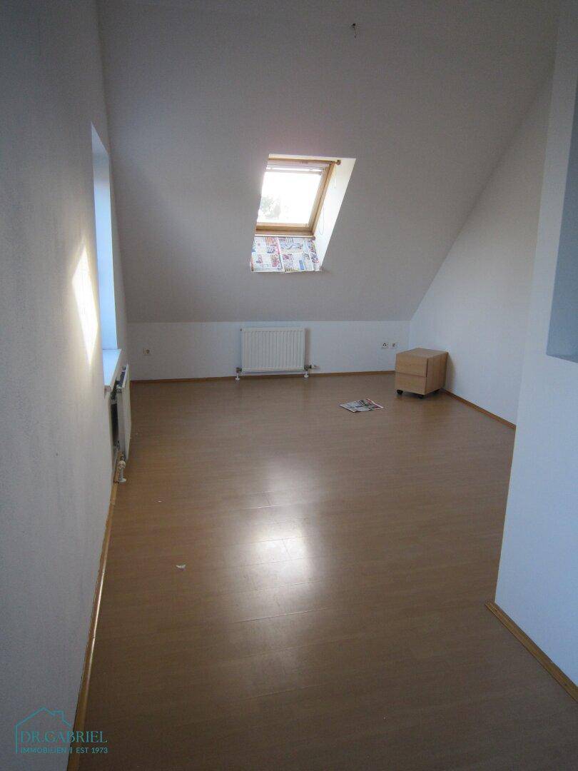Dachzimmer mit Laminatboden, schräger Decke und einem Dachfenster für natürliches Licht.