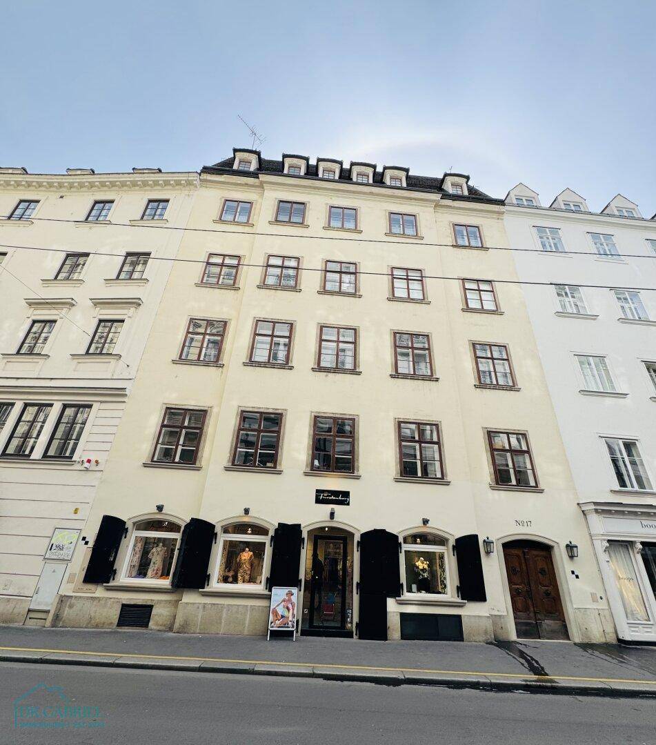 Klassisches Gebäude mit mehreren Stockwerken, vielen Fenstern und Geschäften im Erdgeschoss an einer Straße.