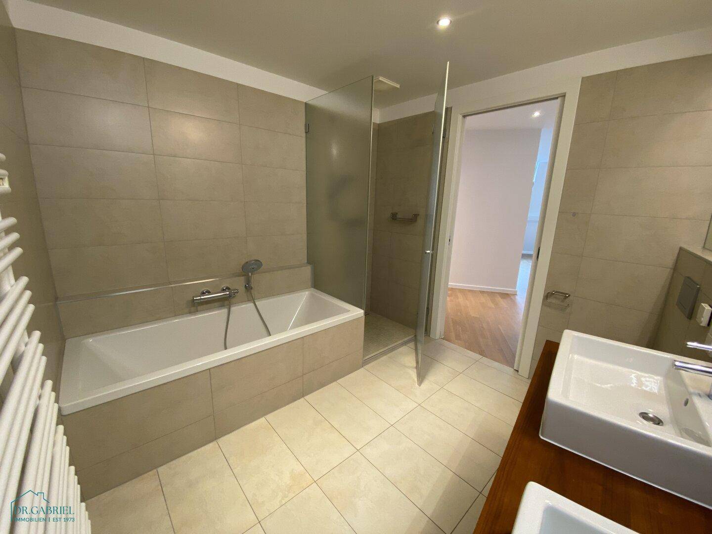 Modernes Badezimmer mit Badewanne, Duschbereich und Doppelwaschbecken auf Holzunterschrank.