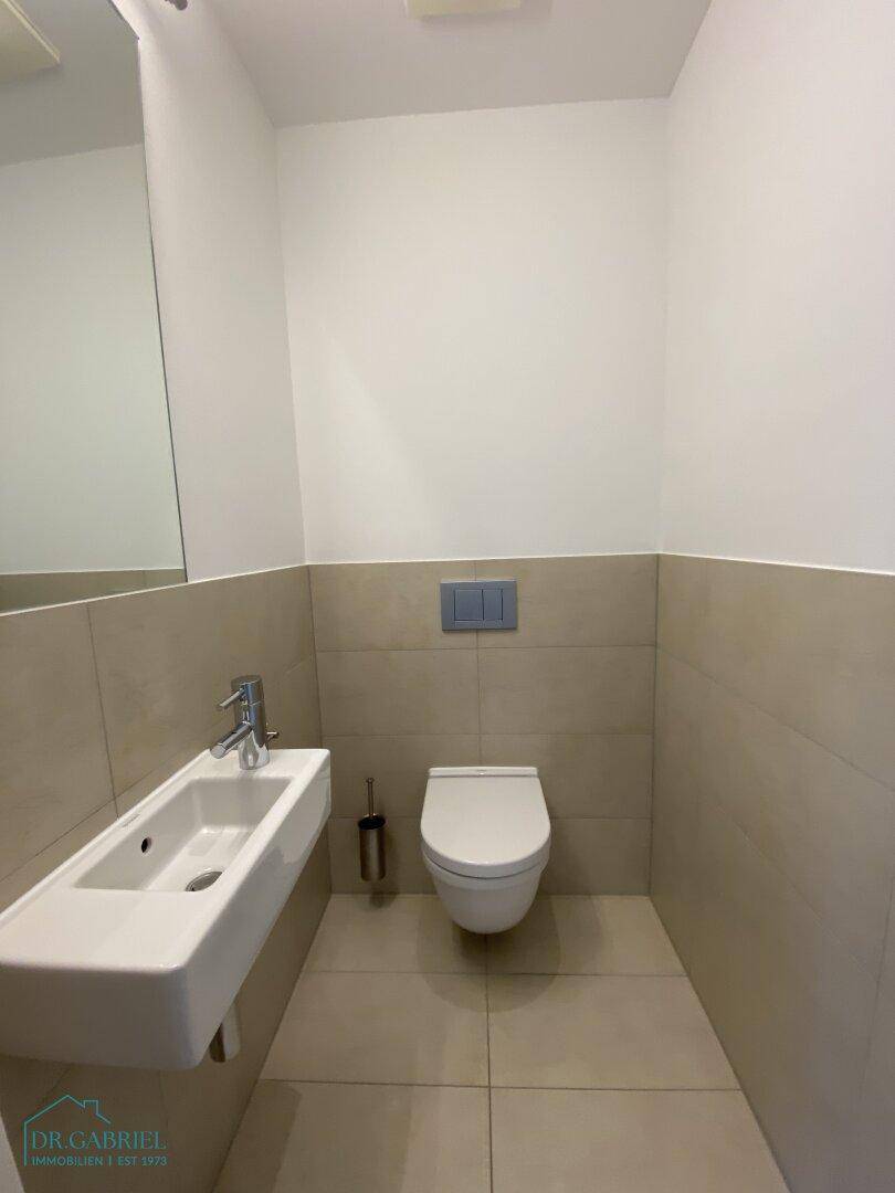 Modernes Gäste-WC mit Wand-WC, kleinem Waschbecken und hellen Fliesen.