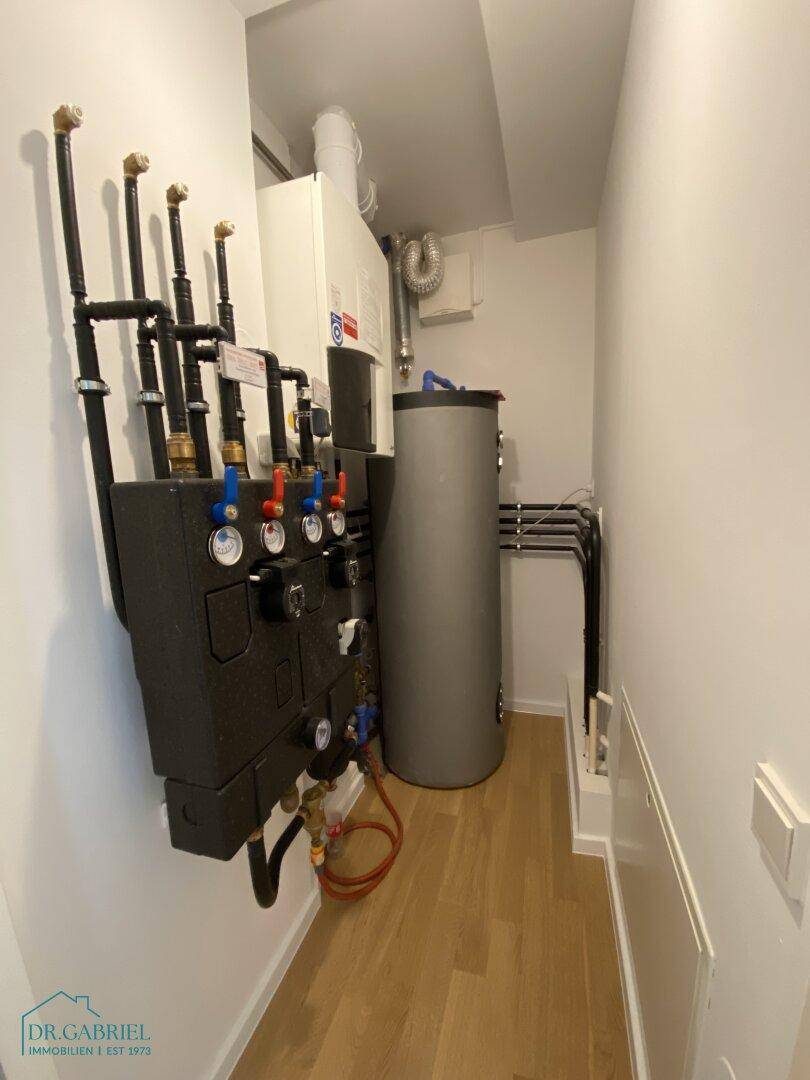Technikraum mit Heizungsanlage, Warmwasserspeicher und zahlreichen Rohrleitungen.