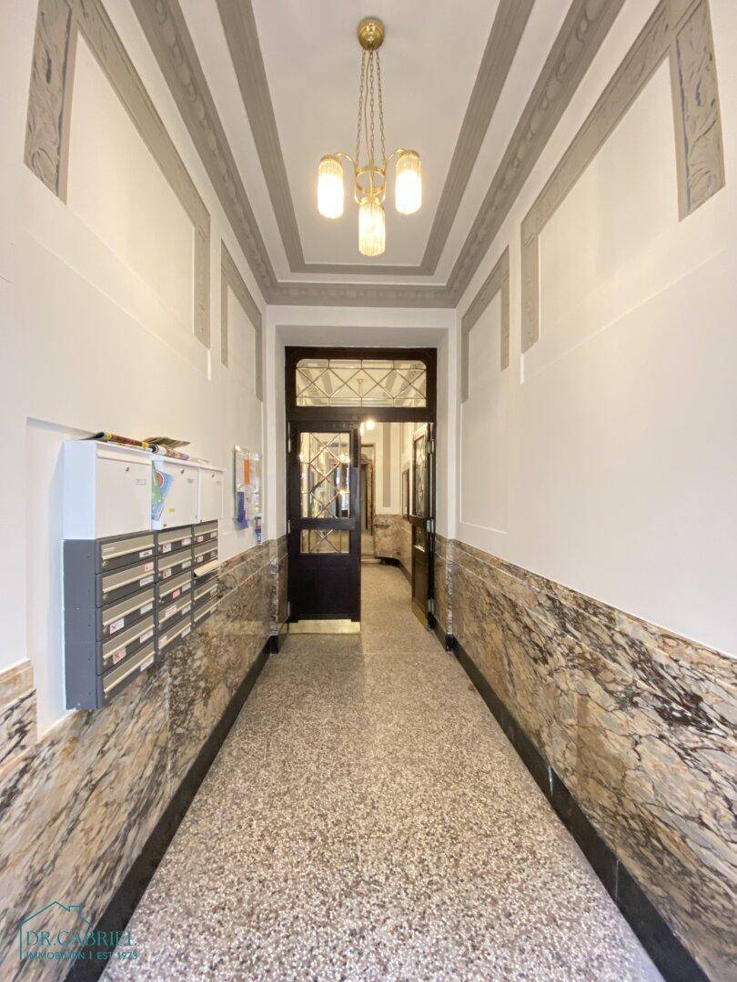 Langer Flur im Altbau mit Marmorverkleidung, Deckenstuck und Briefkästen an der Wand.