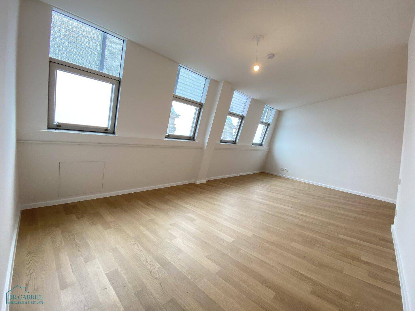 Helles Schlafzimmer mit Holzboden und mehreren schrägen Fenstern, die eine einzigartige Atmosphäre schaffen.