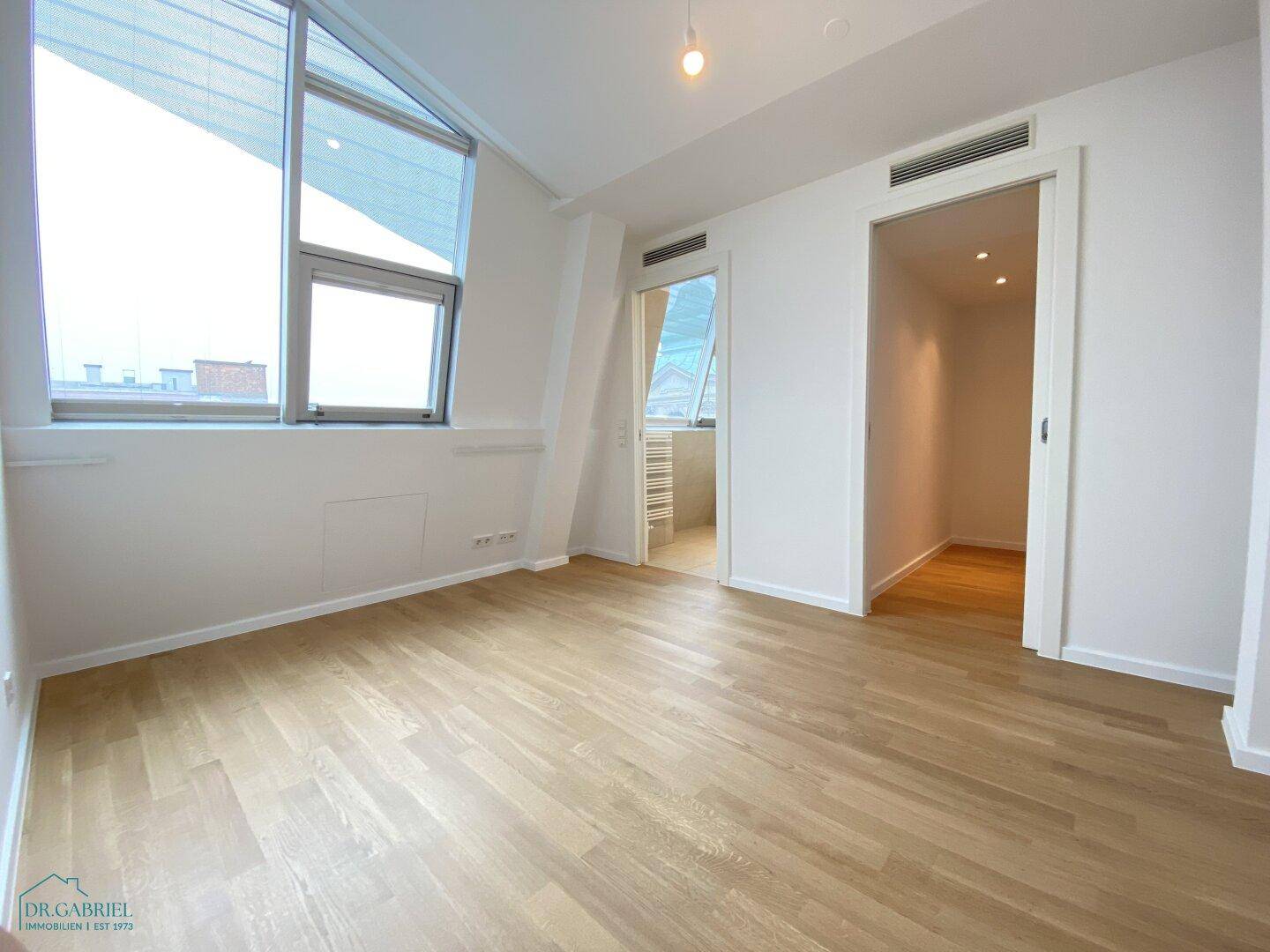 Helles Zimmer mit Holzboden und Zugang zu einem begehbaren Kleiderschrank, ideal als Schlafzimmer.
