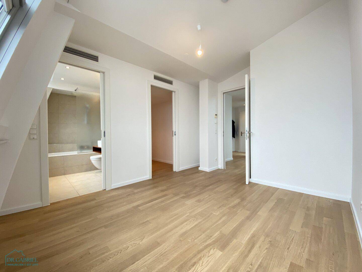 Heller Flurbereich mit Holzboden und Zugang zu einem modernen Badezimmer und weiteren Zimmern.