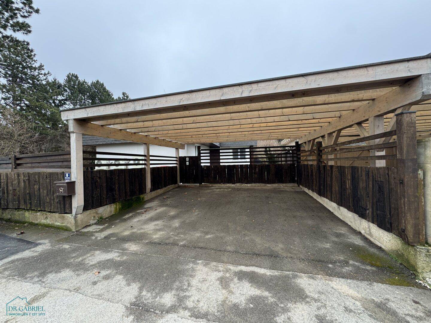 Geräumiger Holzcarport mit offener Konstruktion, bietet Schutz für Fahrzeuge auf dem Grundstück.