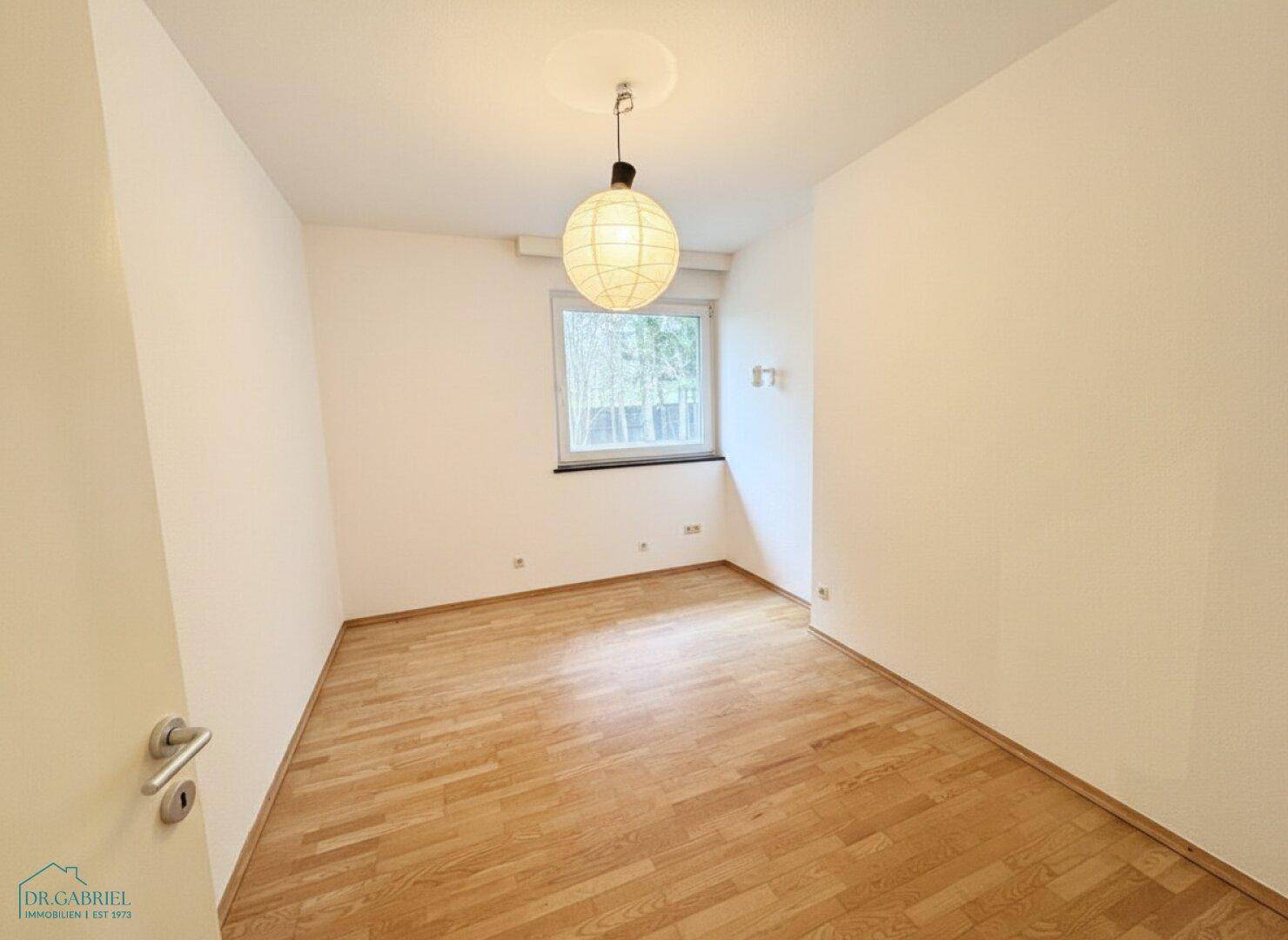 Leerer Raum mit hellem Holzboden und Fenster, vielseitig nutzbar als Büro oder Gästezimmer.