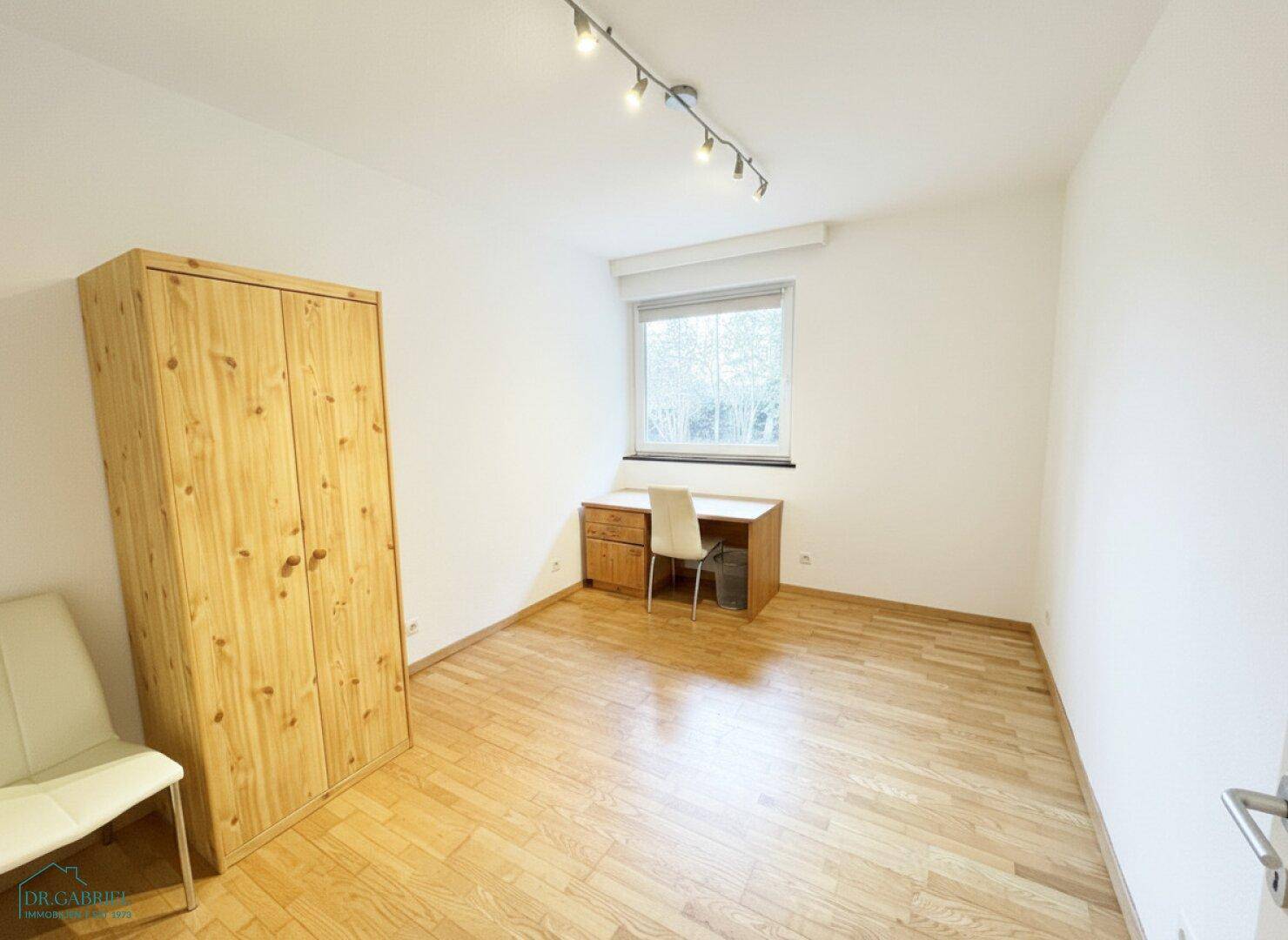 Leeres Schlafzimmer mit hellem Holzboden, Fenster und Holzschrank, bereit zur individuellen Gestaltung.