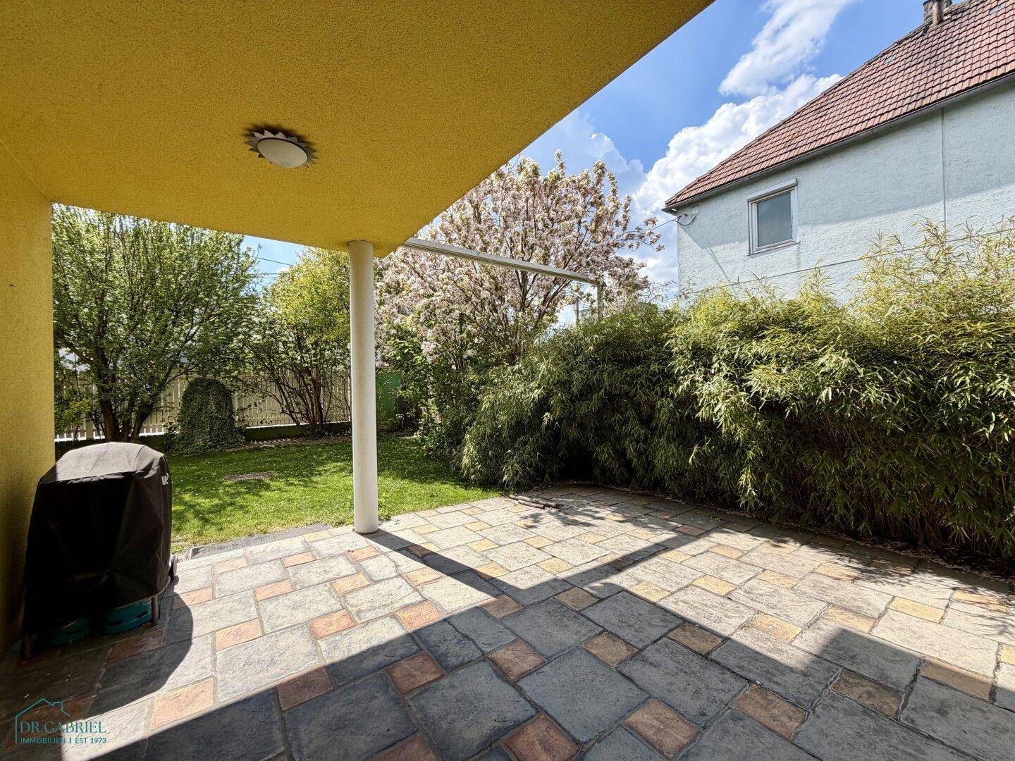 Überdachte Terrasse mit Steinplatten und Blick in den grünen Gartenbereich des Hauses.