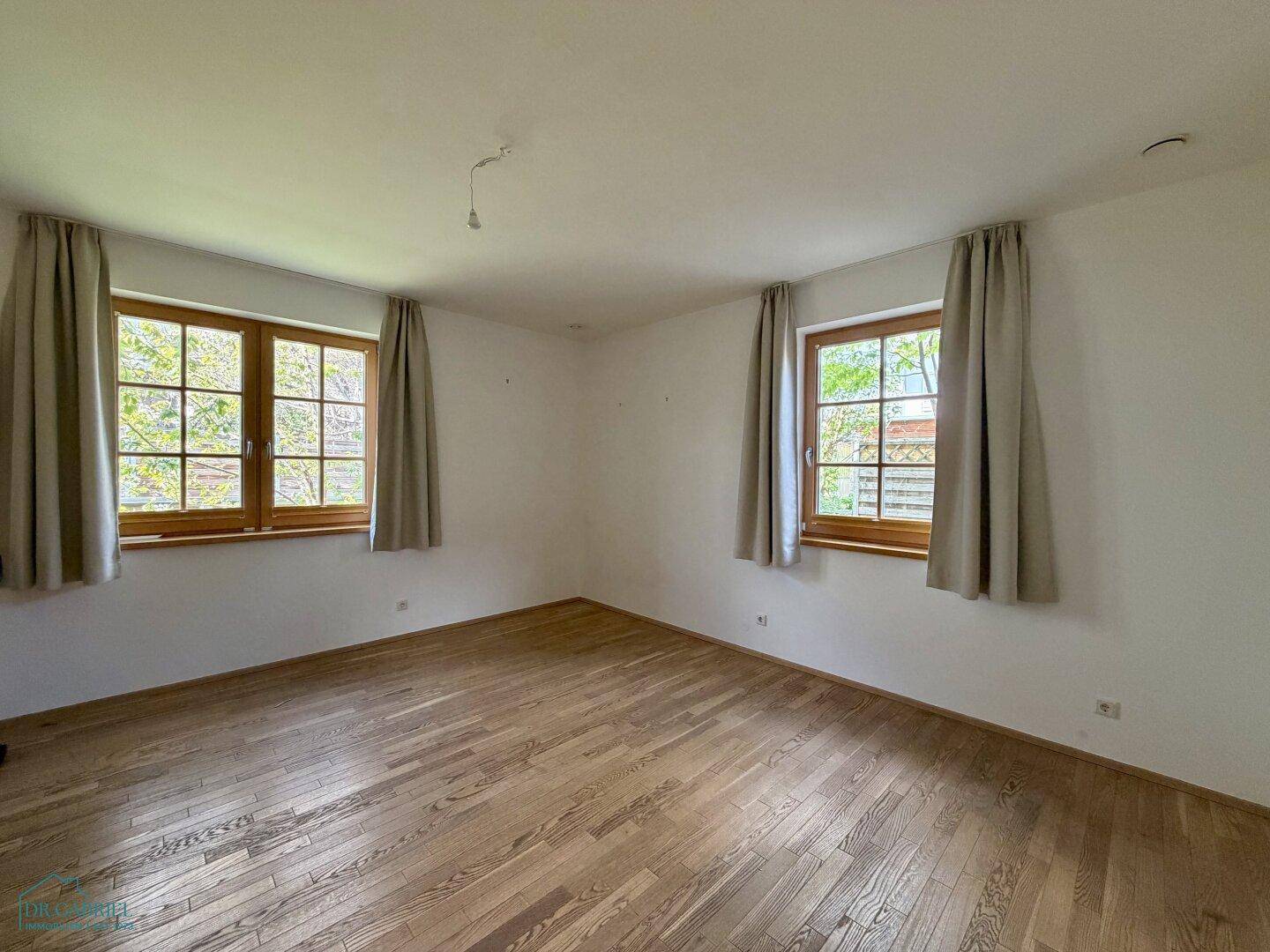 Helles Zimmer mit Holzboden und zwei Fenstern, bereit zur individuellen Gestaltung.
