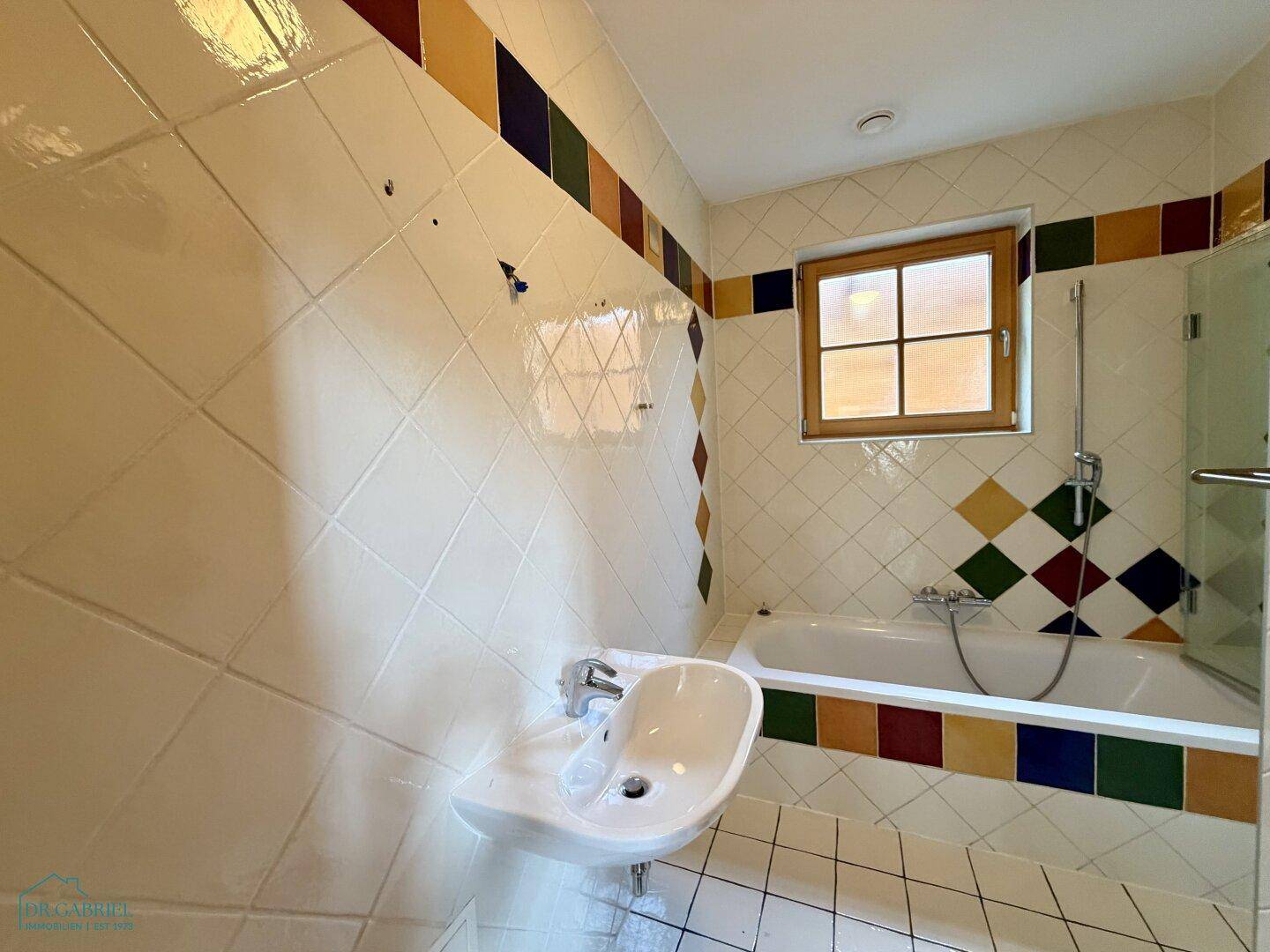 Badezimmer im 80er-Jahre-Stil mit farbigen Fliesen, Badewanne und Einzelwaschbecken.