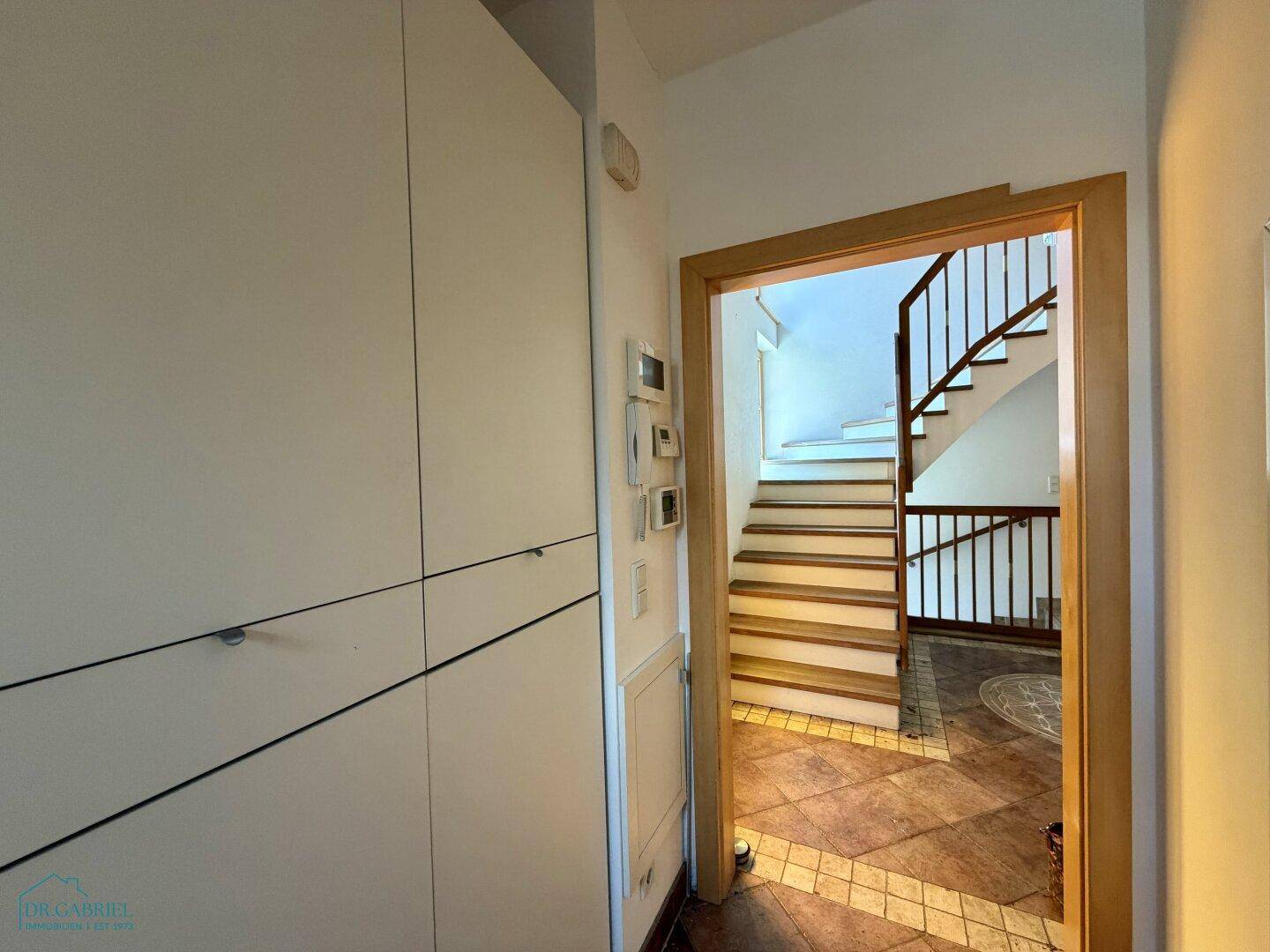 Heller Flur mit Einbauschränken und Blick auf die Holztreppe zum Obergeschoss.