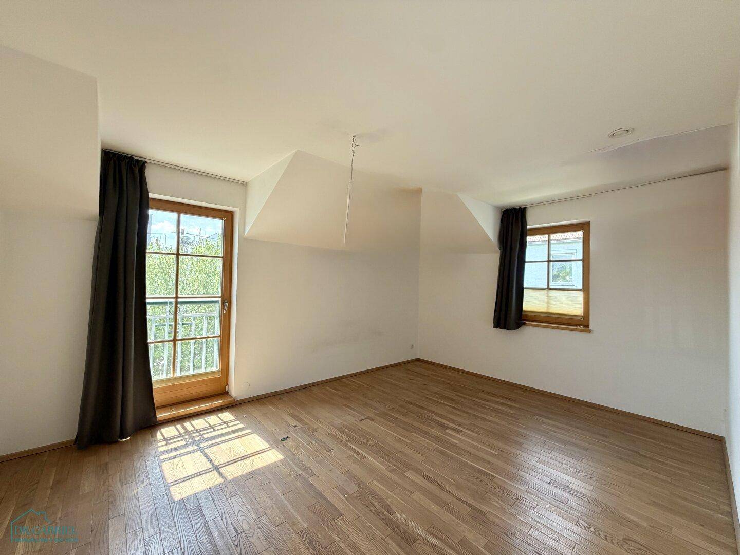 Schlafzimmer im Dachgeschoss mit Holzboden, Dachschrägen und Zugang zu einem französischen Balkon.