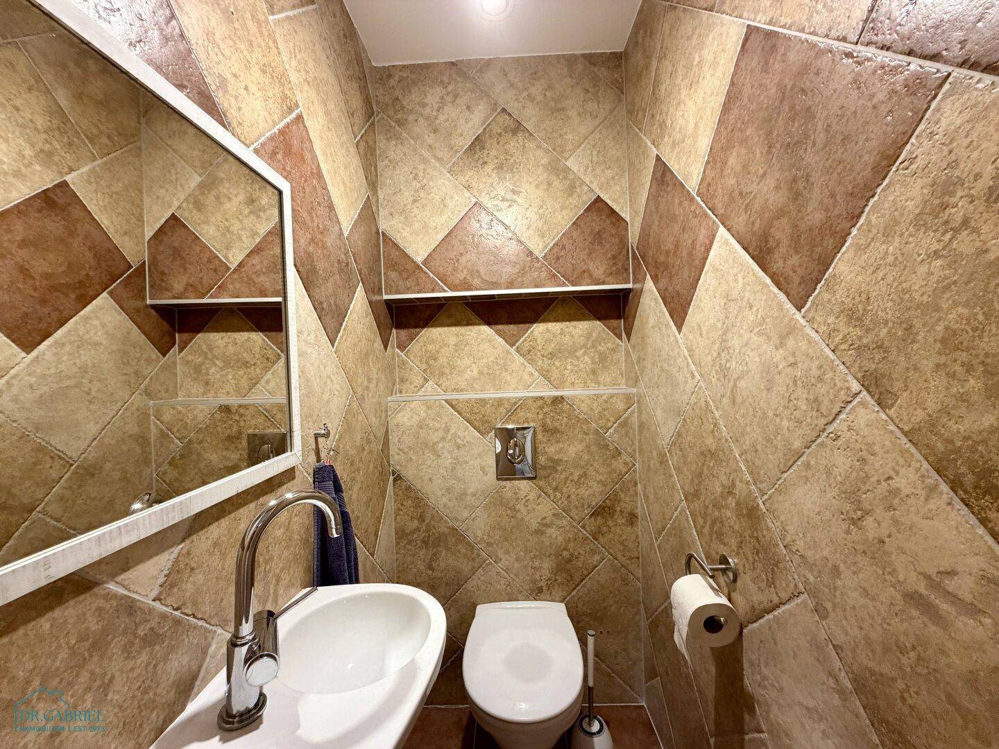 Kleines Gäste-WC mit modernem Waschbecken, Wand-WC und dekorativen Fliesen.