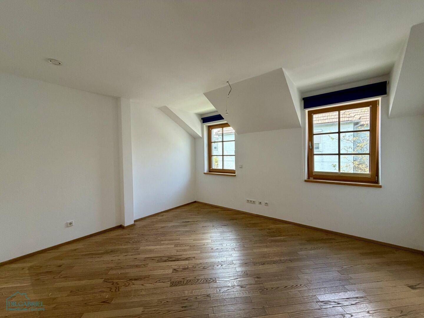 Helles Schlafzimmer im Dachgeschoss mit Holzboden und zwei Fenstern, bietet viel Tageslicht.