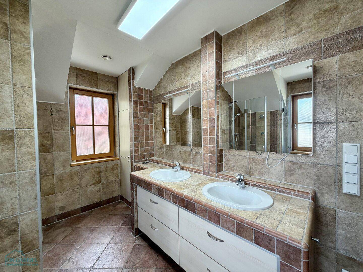 Geräumiges Badezimmer mit Doppelwaschbecken, Fliesenboden und Dachfenster für natürliches Licht.