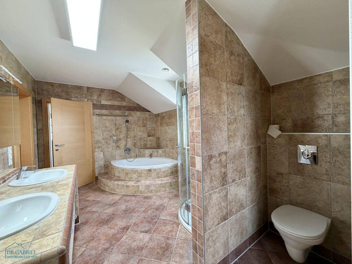Modernes Badezimmer mit Doppelwaschbecken, Dusche und WC, komplett gefliest.
