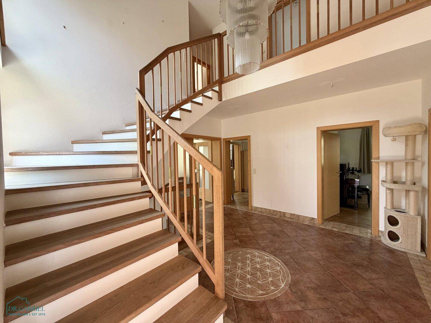Geräumiger Eingangsbereich mit eleganter Holztreppe und Fliesenboden, lichtdurchflutet.