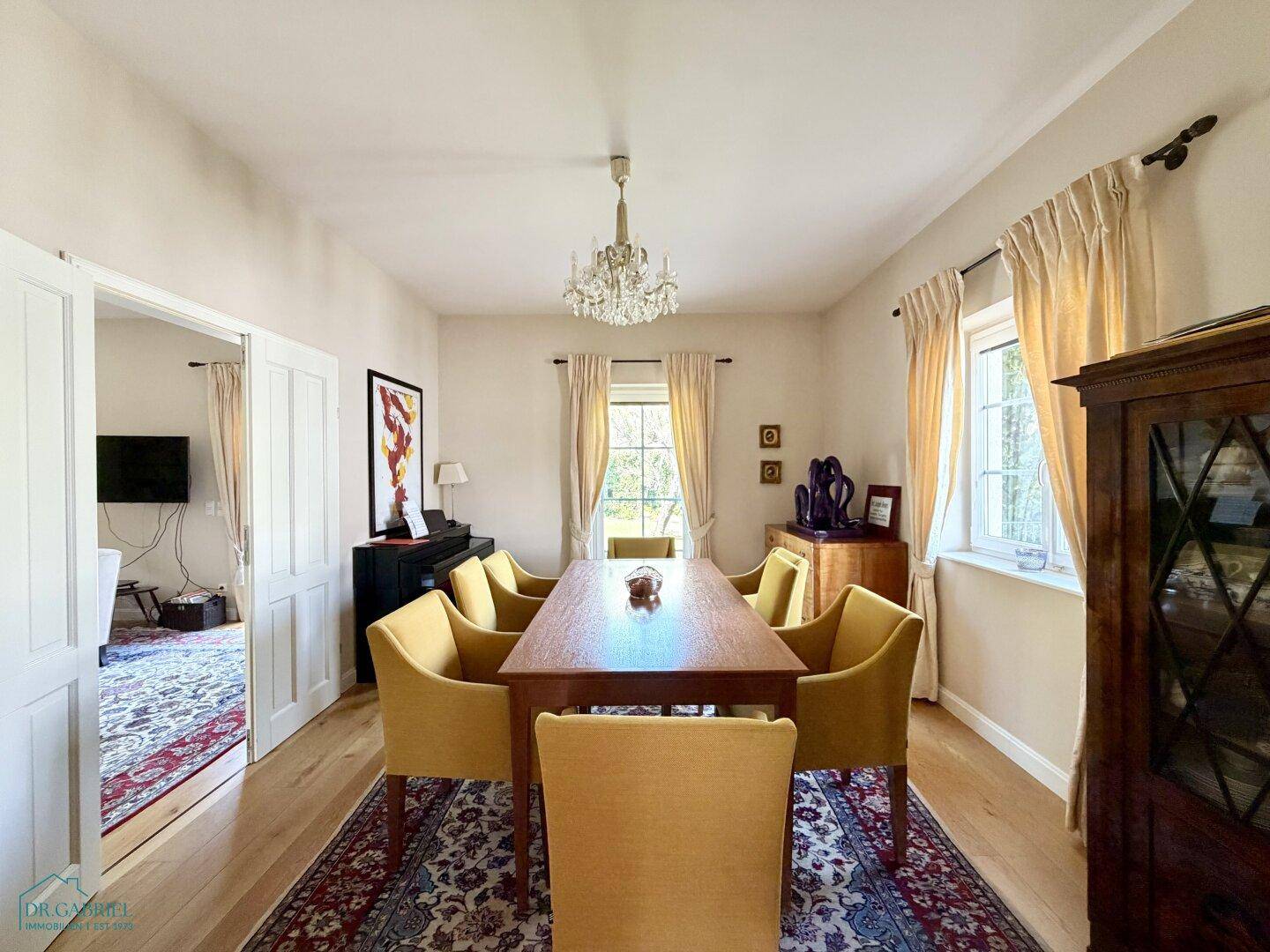 Stilvolles Esszimmer mit Holztisch, gelben Stühlen und Kronleuchter, verbunden mit dem Wohnbereich.