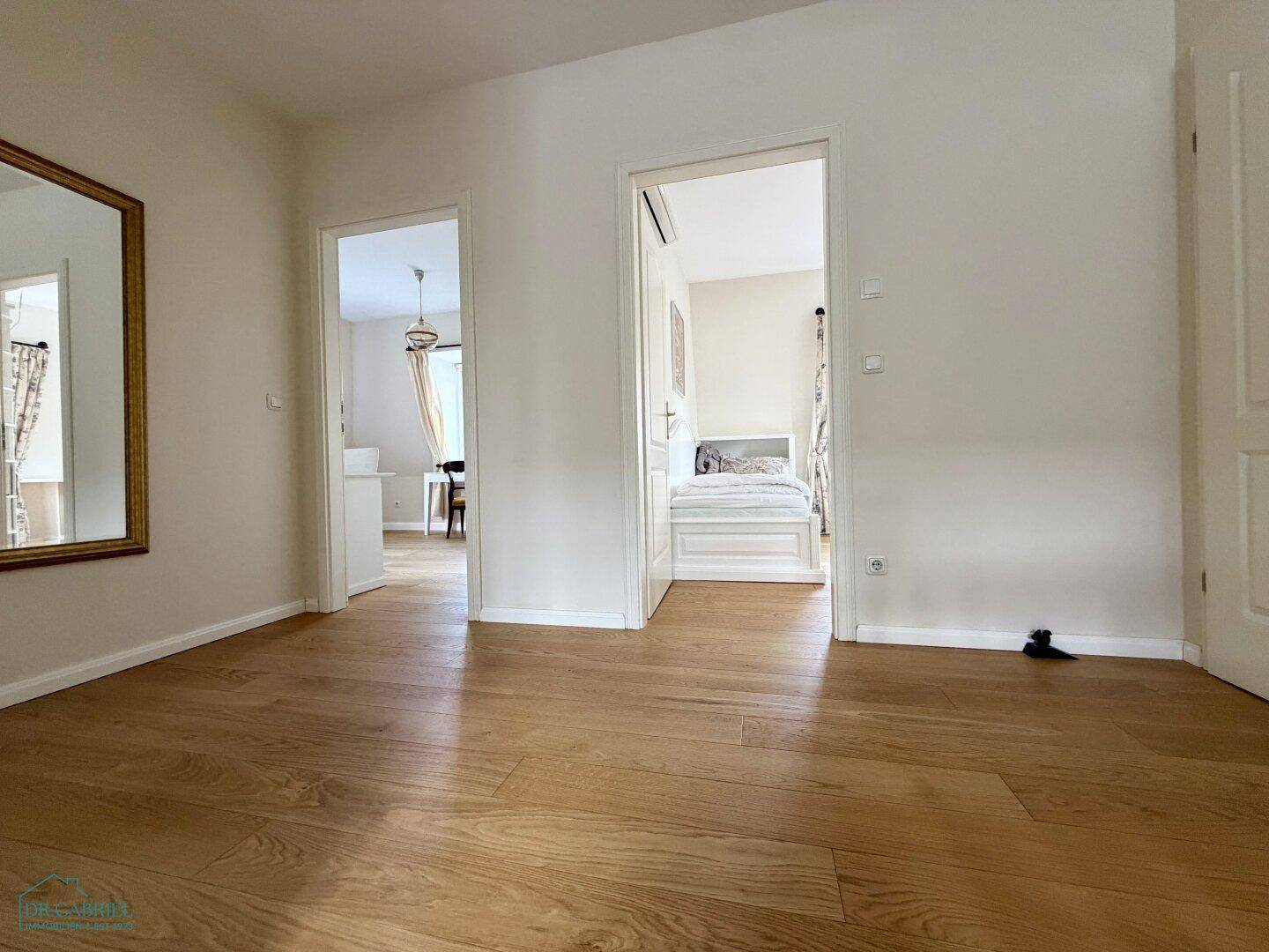 Heller Raum mit Holzboden und Türen zu angrenzenden Zimmern, bereit zur individuellen Gestaltung.