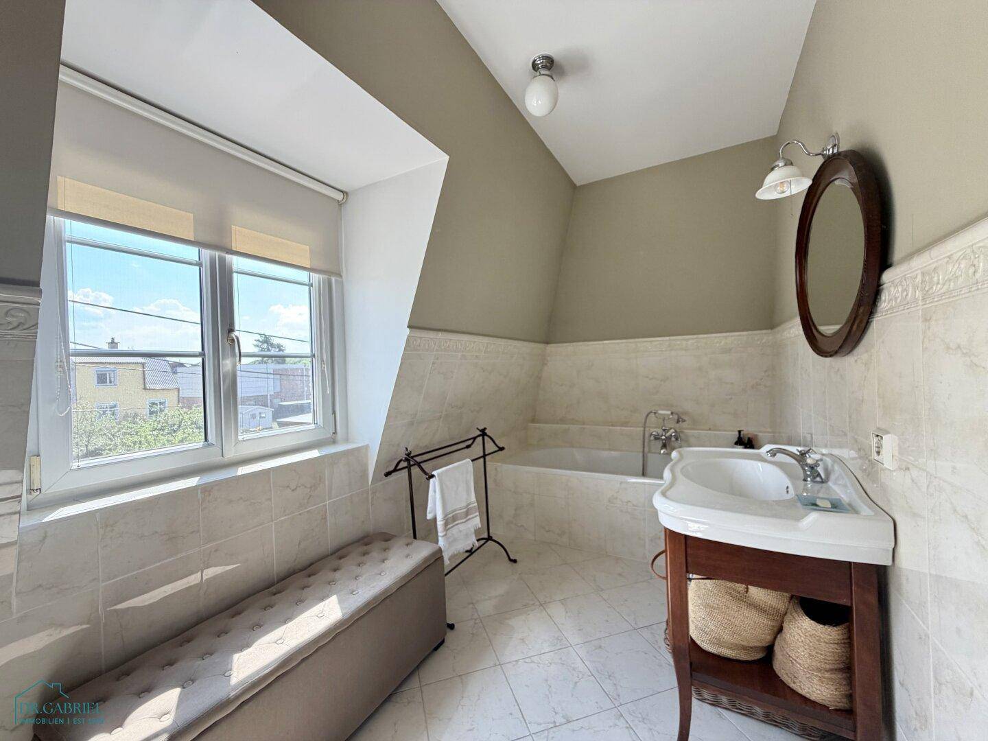 Geräumiges Badezimmer mit Badewanne, Waschtisch und Fenster, unter einer Dachschräge gelegen.