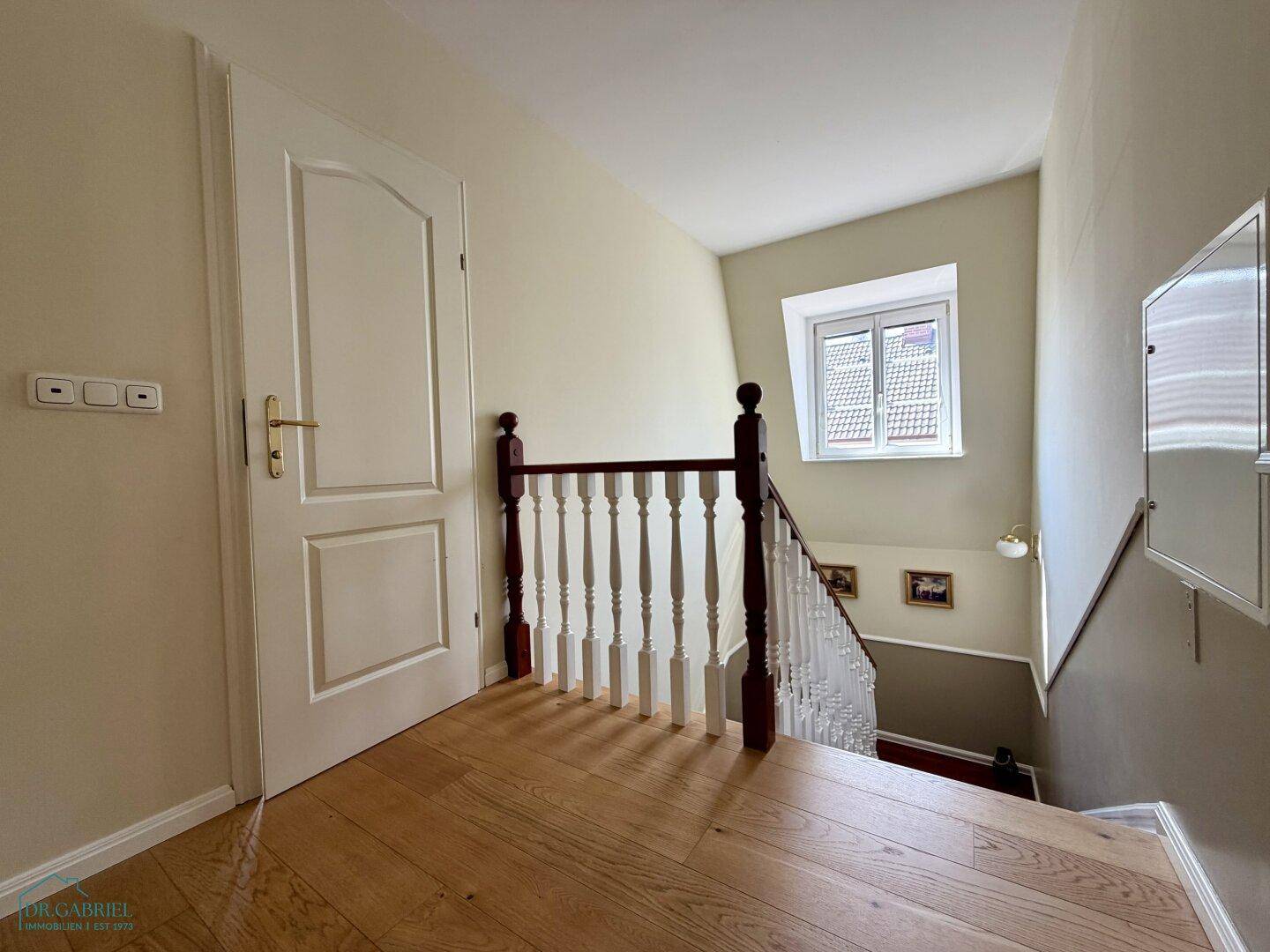 Heller Treppenabsatz mit Holzboden und Fenster, das Tageslicht in den oberen Bereich bringt.