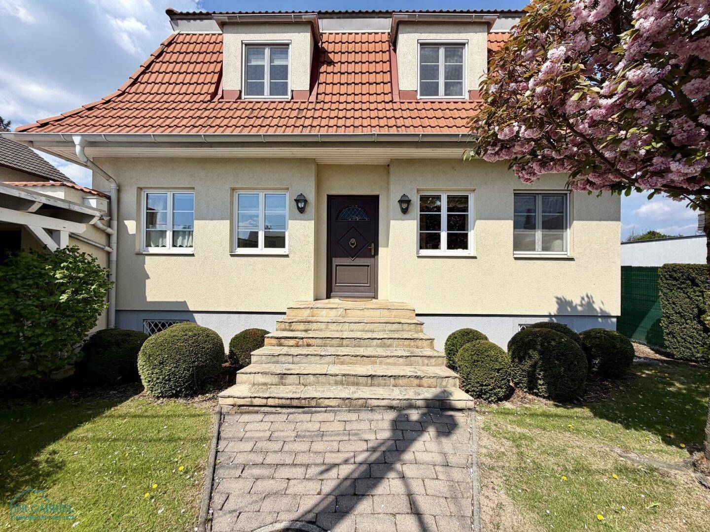 Traditionelles Einfamilienhaus mit Walmdach, gepflegtem Vorgarten und Steintreppe zum Eingang.