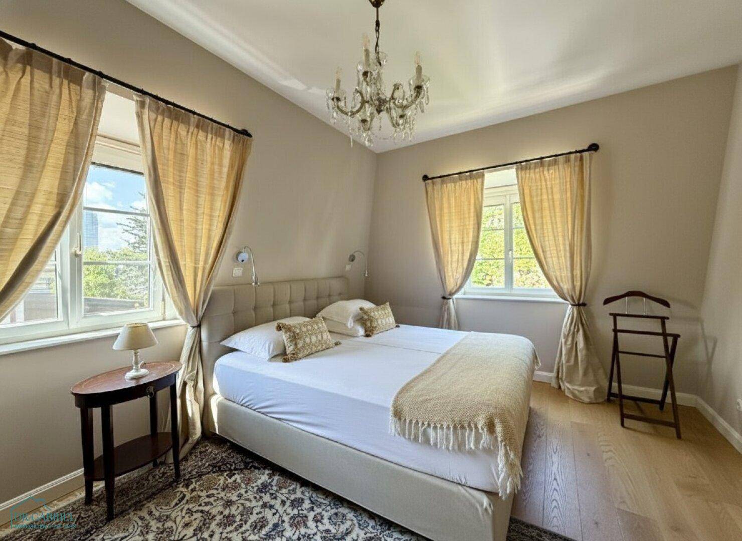 Gemütliches Schlafzimmer mit Doppelbett, Holzboden und zwei Fenstern für viel Tageslicht.