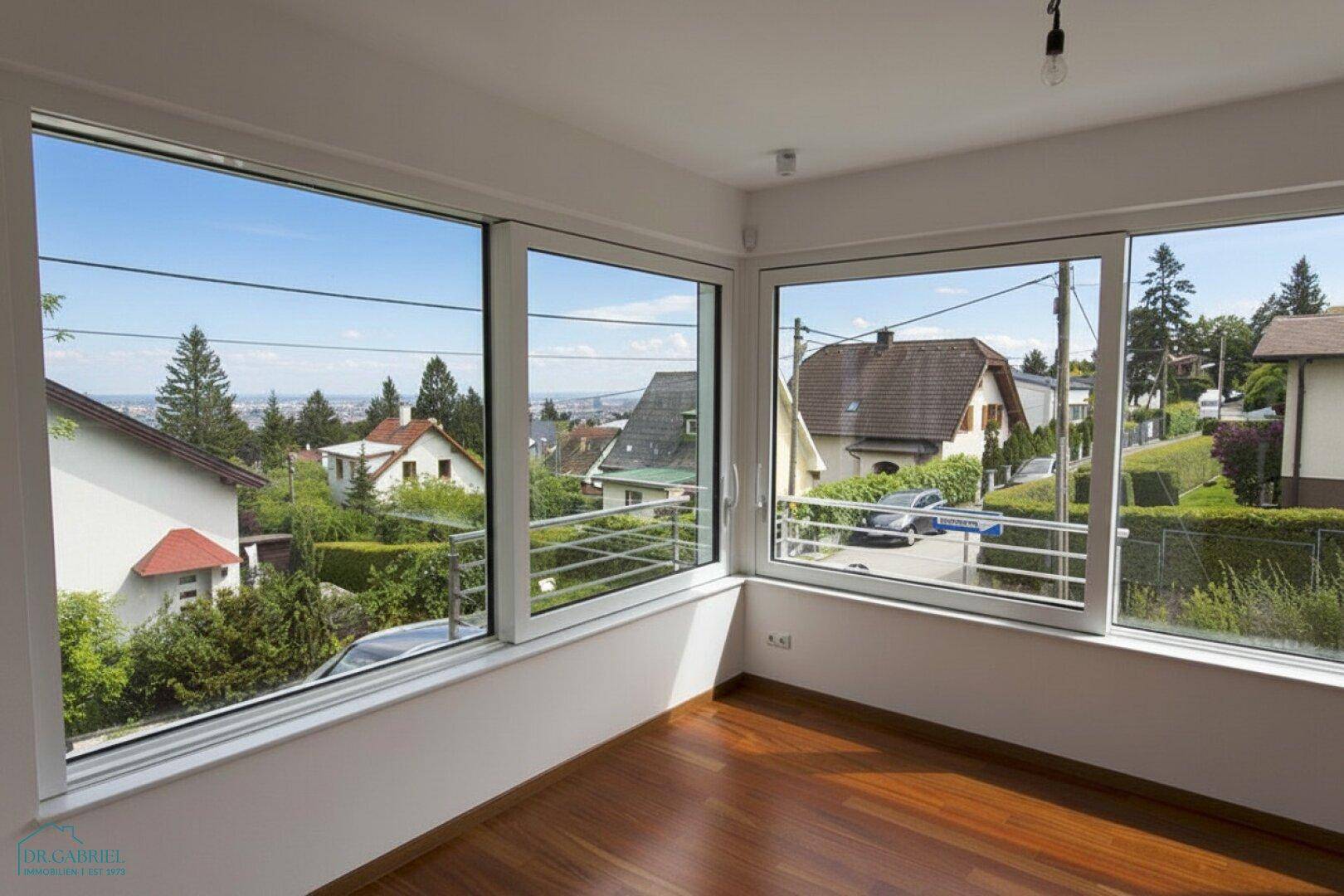 Heller Raum mit Holzboden und großen Fenstern, die einen weiten Blick über die Stadt bieten.