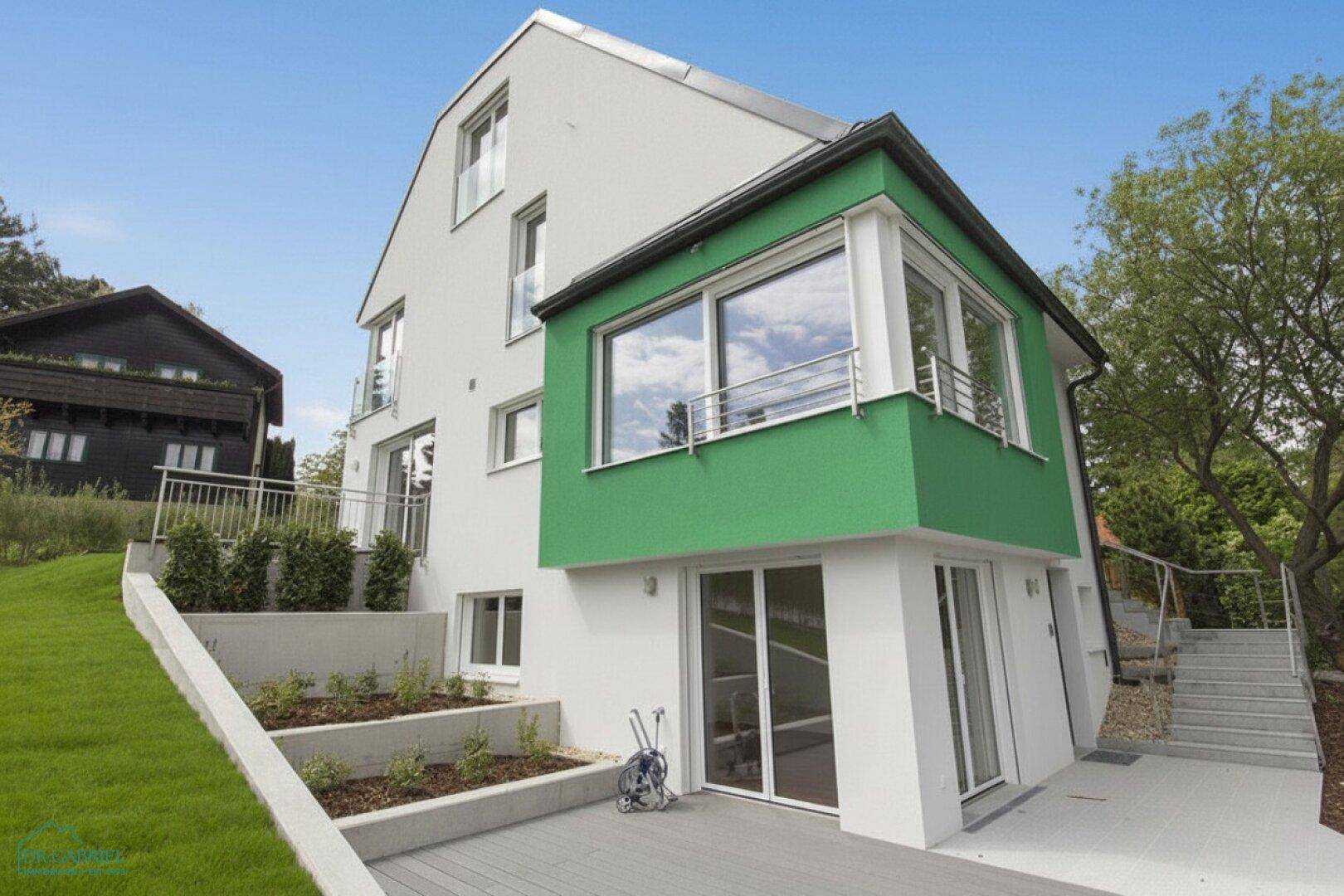 Moderne Hausfassade mit grünen Akzenten, Terrasse und terrassierten Gartenbeeten.