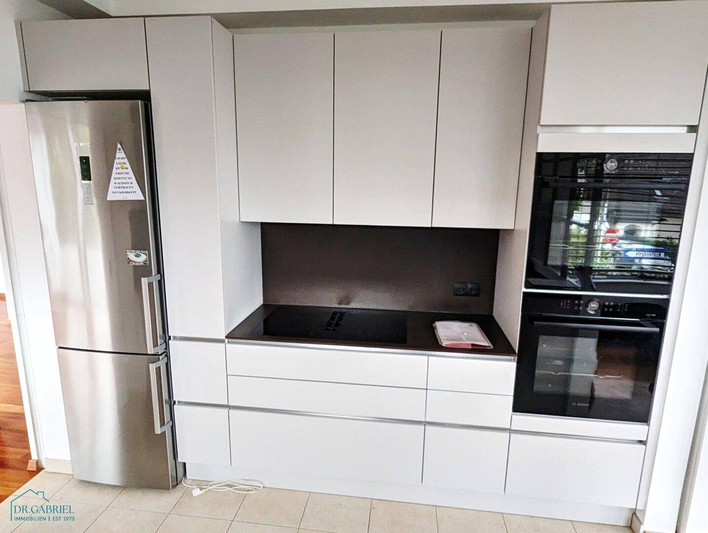 Funktionale Küche mit weißen Schränken, integrierten Geräten und großem Kühlschrank.