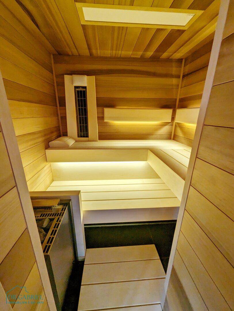 Moderne Sauna aus hellem Holz mit mehrstufigen Bänken und indirekter Beleuchtung.
