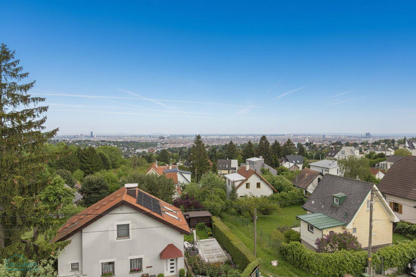 Weitläufiger Blick über eine grüne Wohngegend mit vielen Häusern und Stadtsilhouette am Horizont.