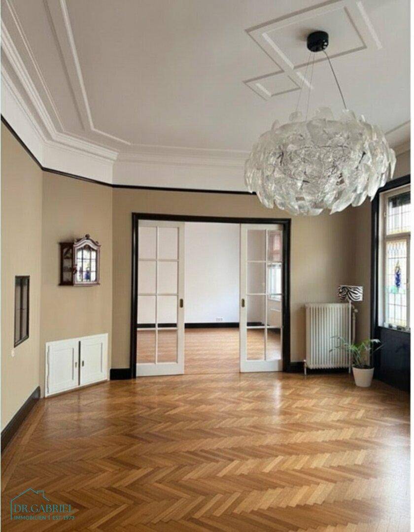 Elegantes Zimmer mit Fischgrätparkett, hohen Stuckdecken und einer modernen Designer-Pendelleuchte.