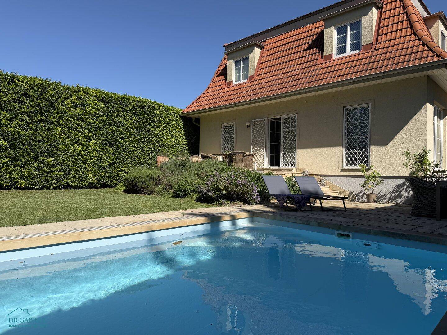 Sonniger Garten mit erfrischendem Pool und Liegeflächen, umgeben von einer hohen grünen Hecke.