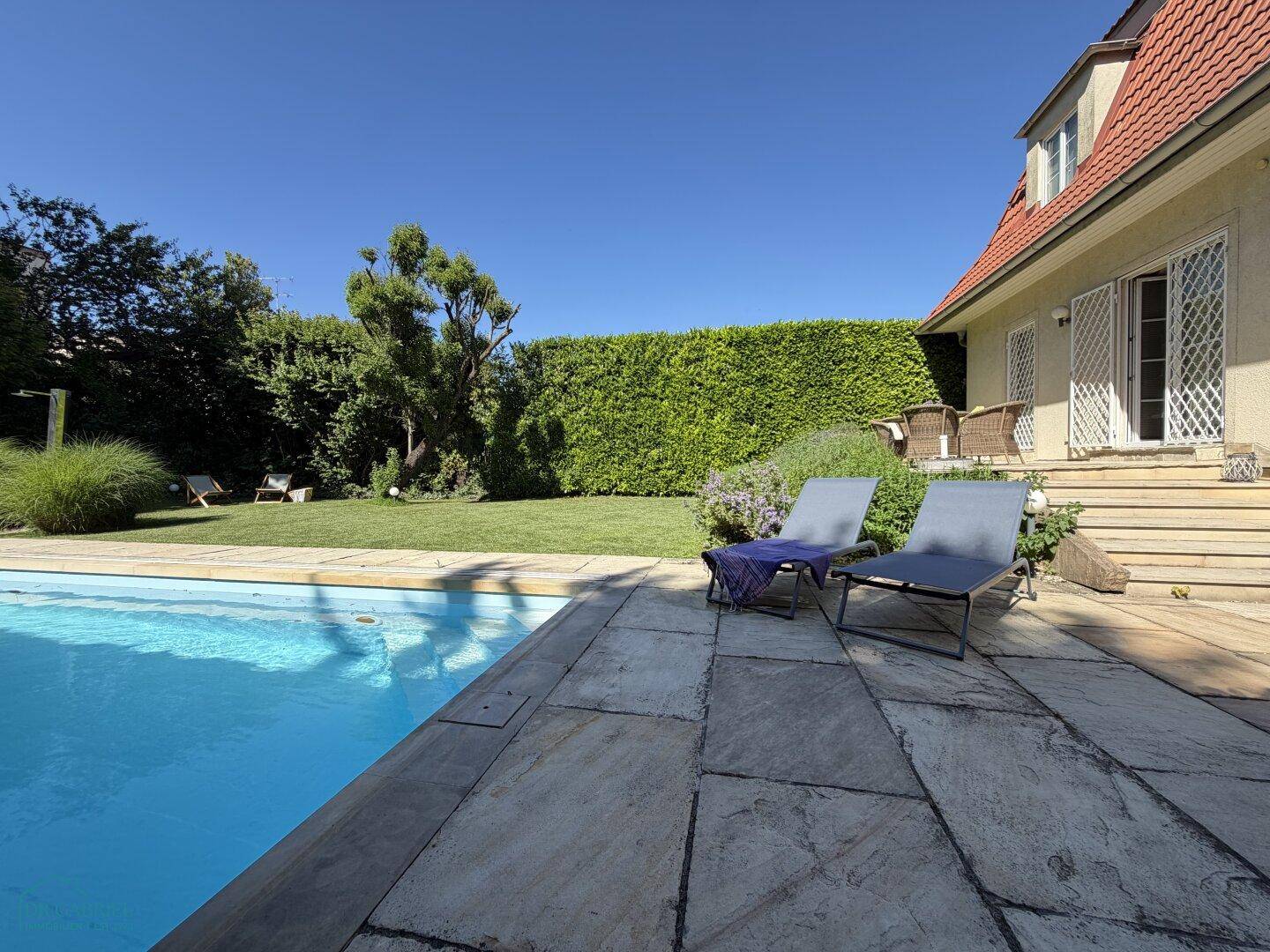 Entspannungsbereich am Pool mit bequemen Liegestühlen auf der sonnigen Steinterrasse im Garten.