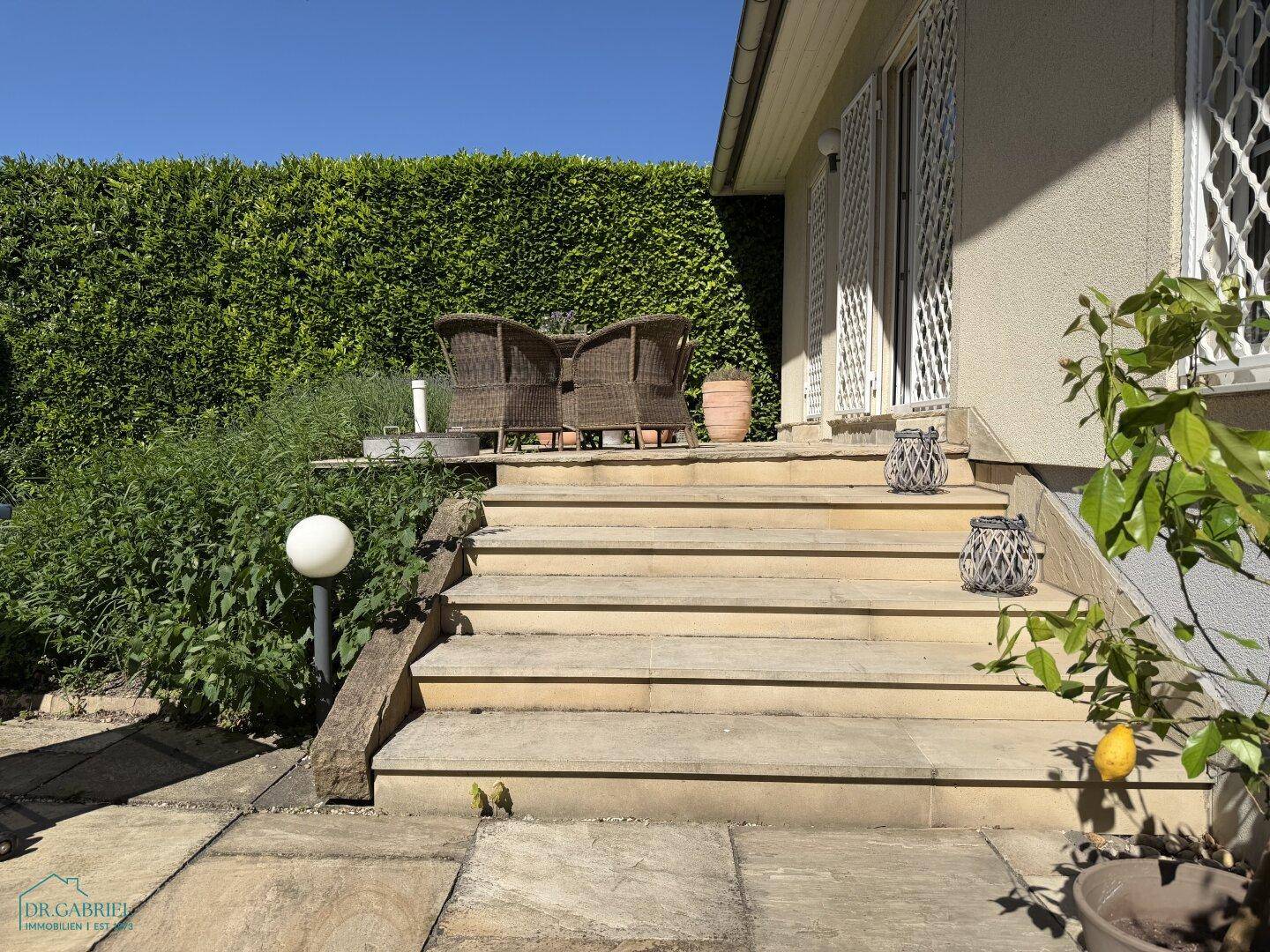 Steintreppe führt vom Garten zur erhöhten Terrasse des Hauses, umgeben von mediterranen Pflanzen.