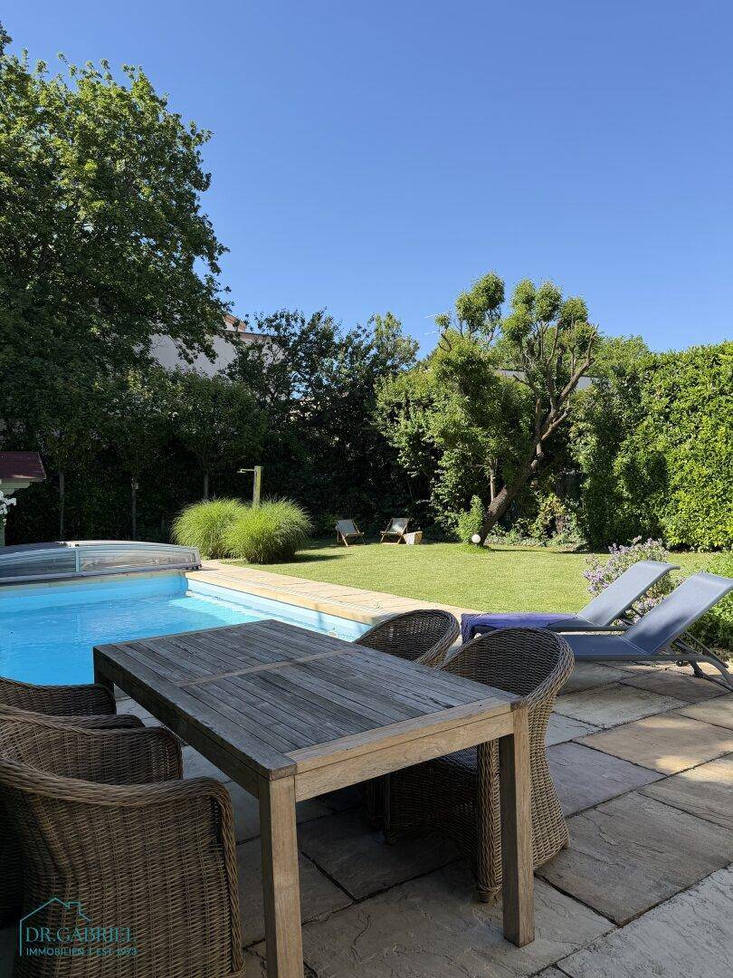 Gemütlicher Essbereich im Freien auf der Steinterrasse neben dem Pool, umgeben von viel Grün.