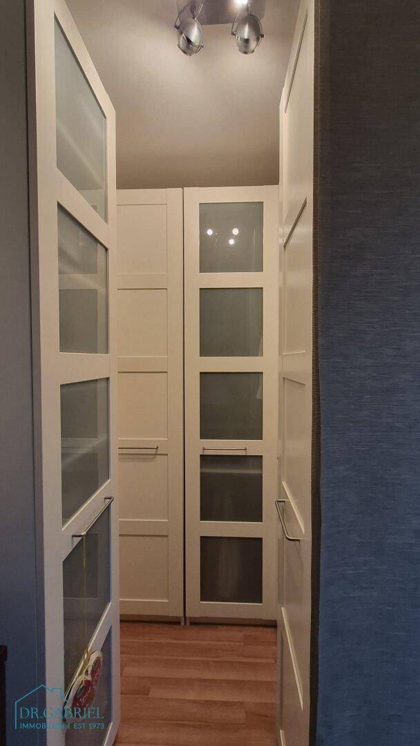 Praktischer begehbarer Kleiderschrank mit weißen Schränken und Holzboden.