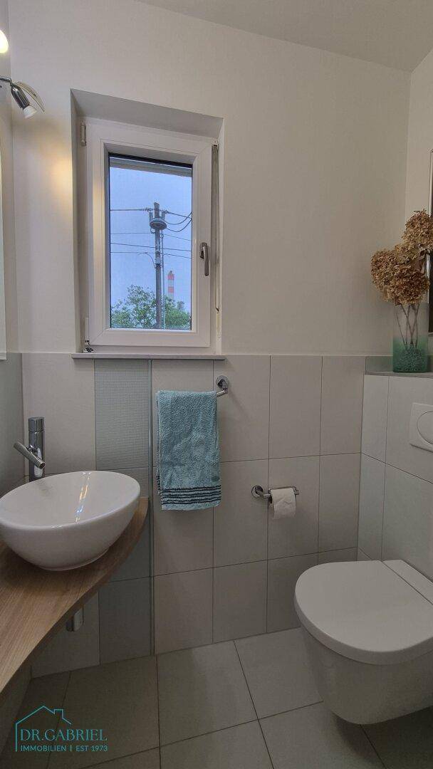 Modernes Gäste-WC mit Waschbecken, Toilette und Fenster, hell gefliest.