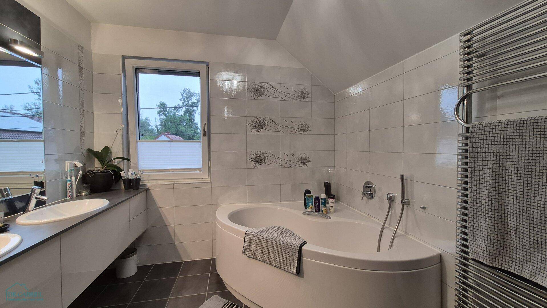 Helles Badezimmer mit Eckbadewanne, Doppelwaschbecken und beheiztem Handtuchhalter.