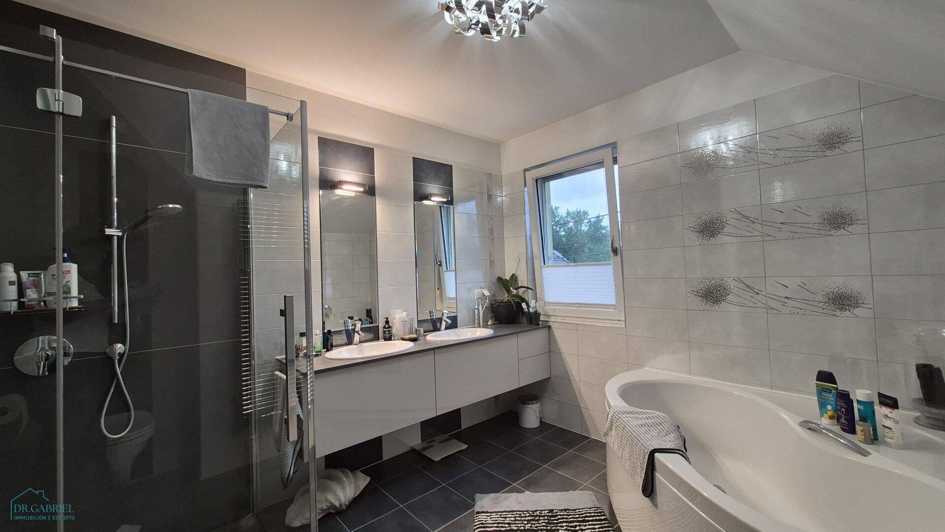Modernes Badezimmer mit Doppelwaschbecken, großer Dusche und Eckbadewanne, hell gefliest.