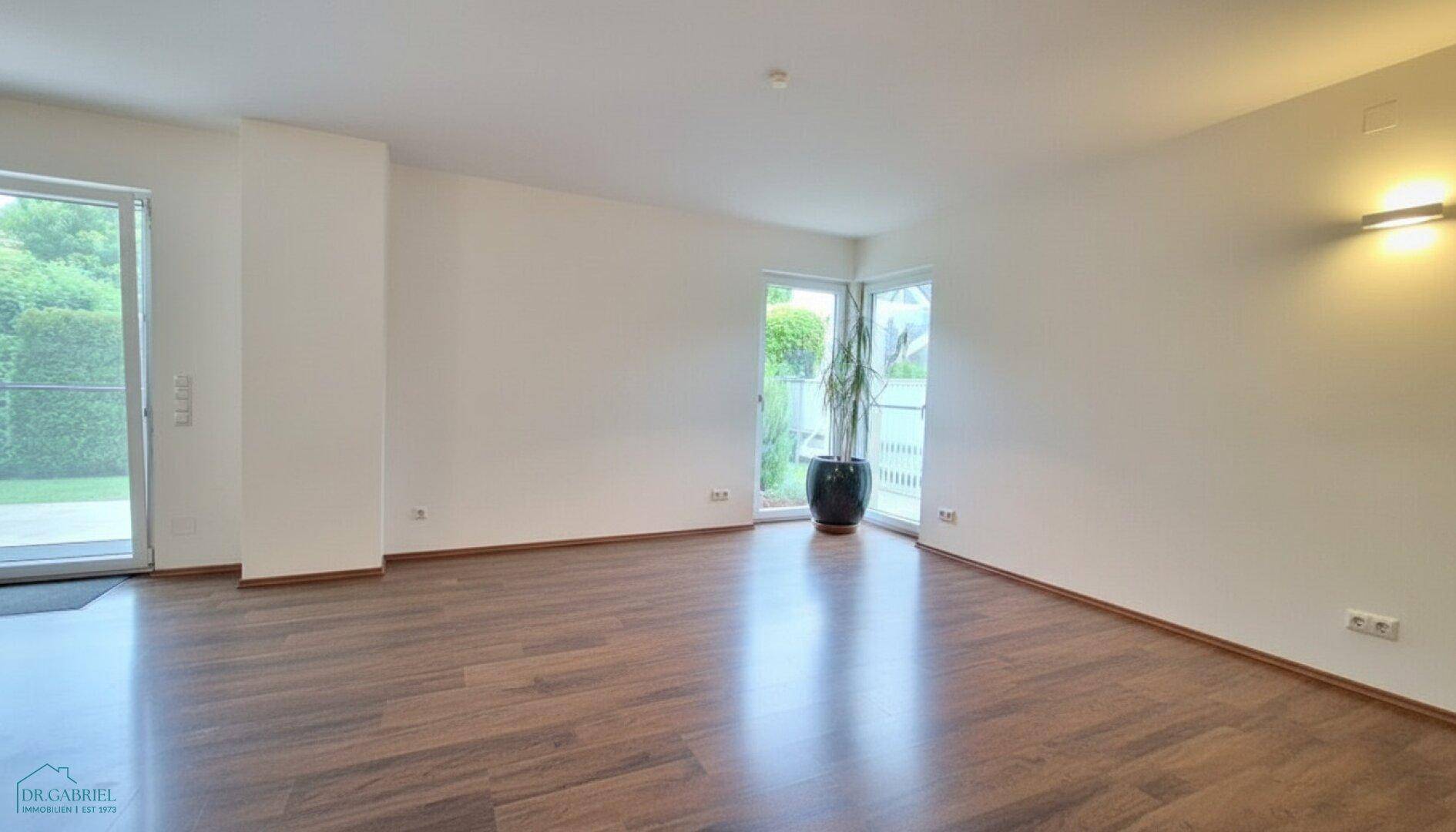 Helles, leeres Wohnzimmer mit Holzboden und Zugang zum Garten durch große Glastüren.