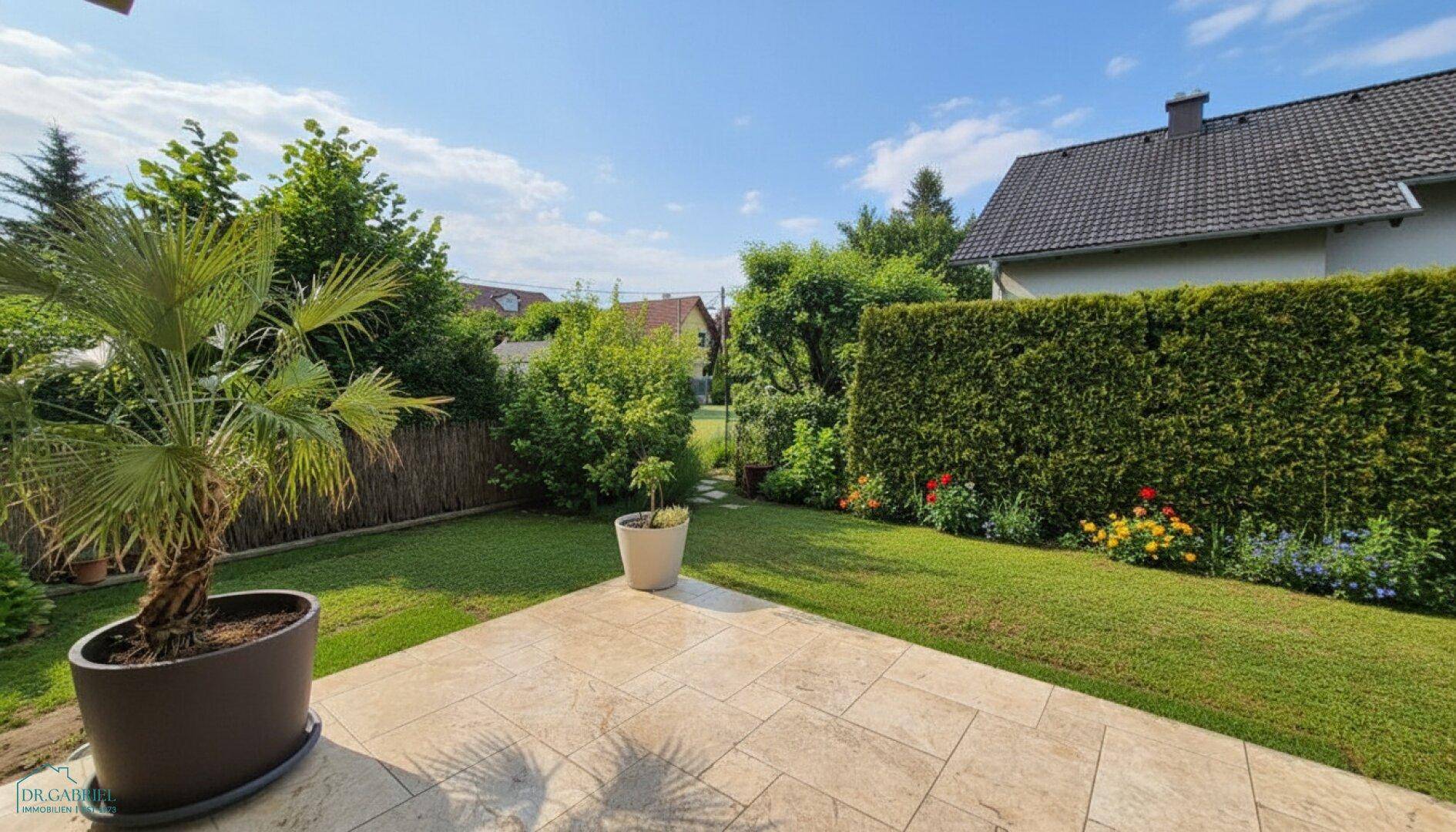 Gepflegter Garten mit Rasenfläche, Blumenbeeten und einer sonnigen Terrasse.